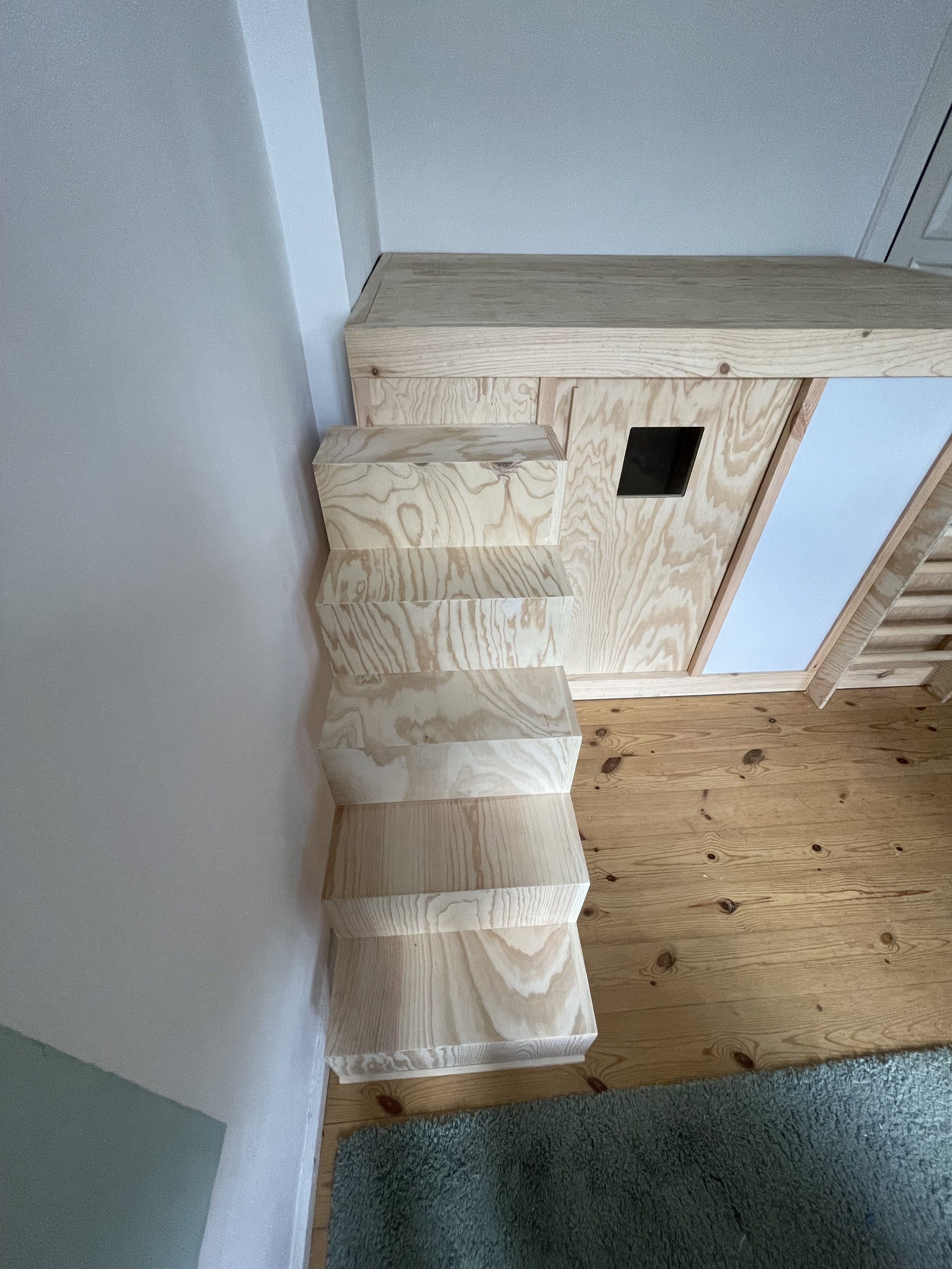Holz-Klapptisch, der flach an der Wand liegt, und ein kleiner Holzstuhl neben einem Bodenbelag aus Holz, in einem Raum mit weiße und holzverkleideter Wand.
