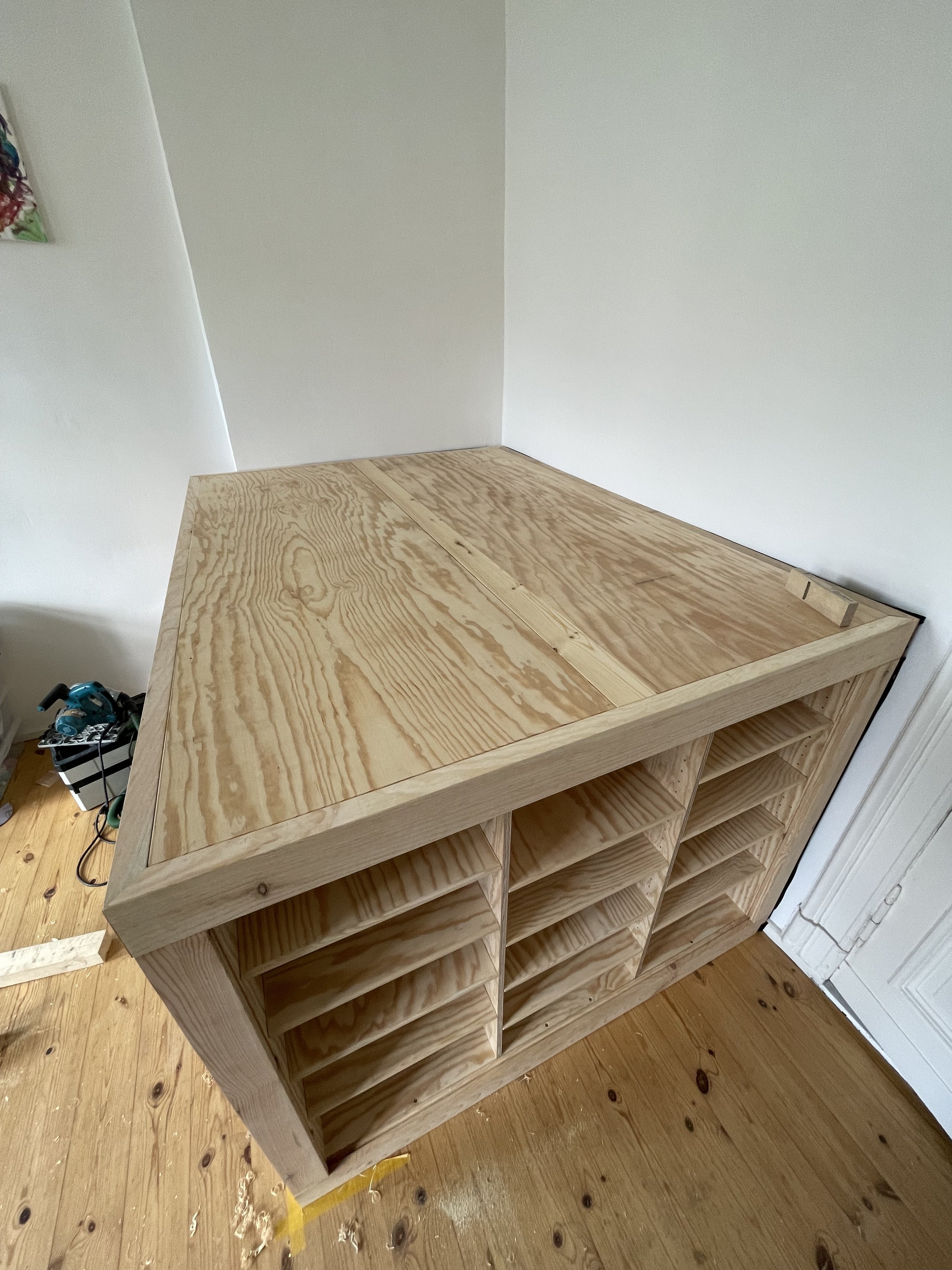 Unfertiger Holzschrank mit offenen Fächern in einem Raum mit Holzboden.
