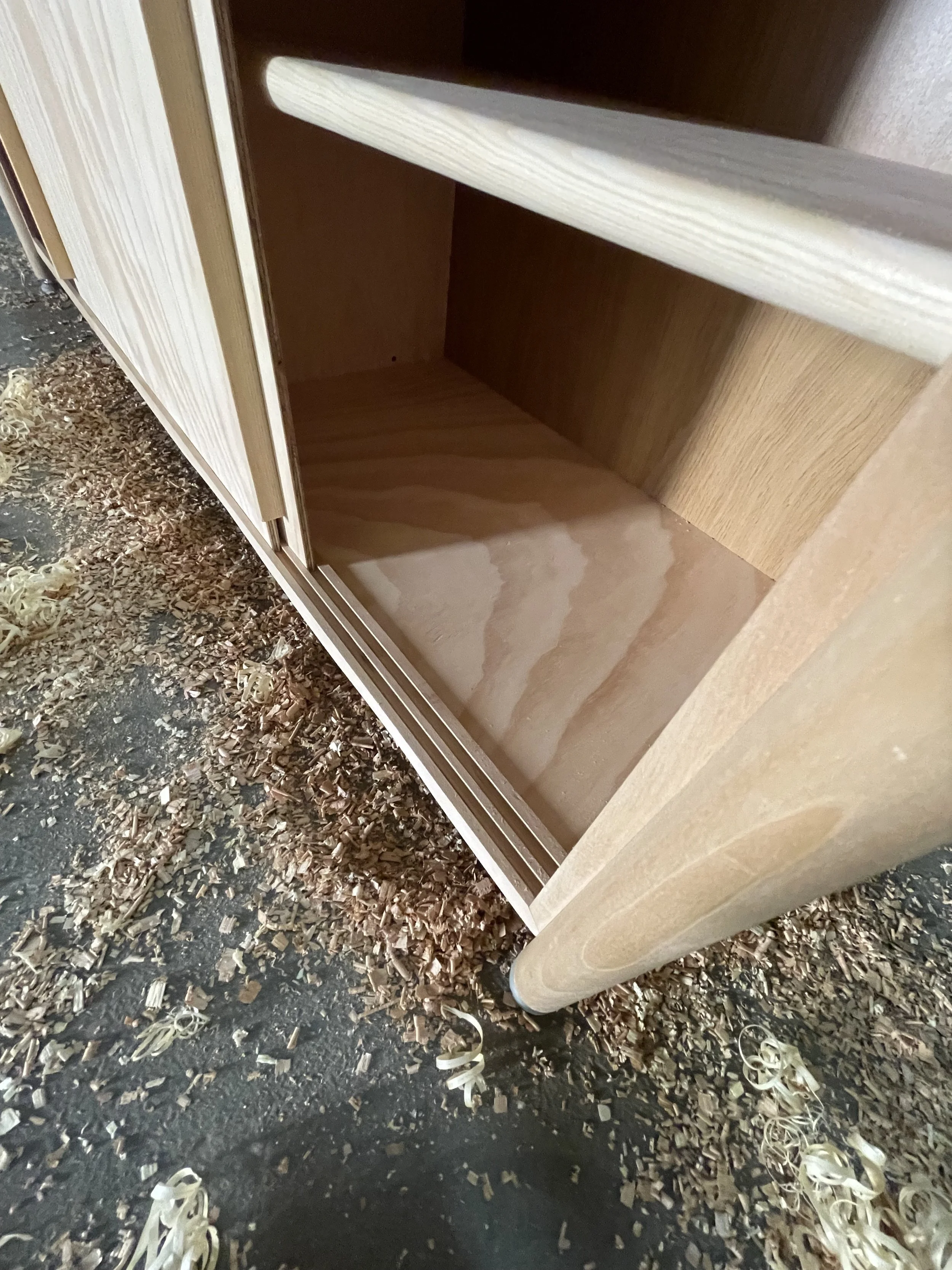 Innenseite eines leeren, ungefütterten Holzkastens, der auf einer Werkstattböden mit Holzspänen steht.