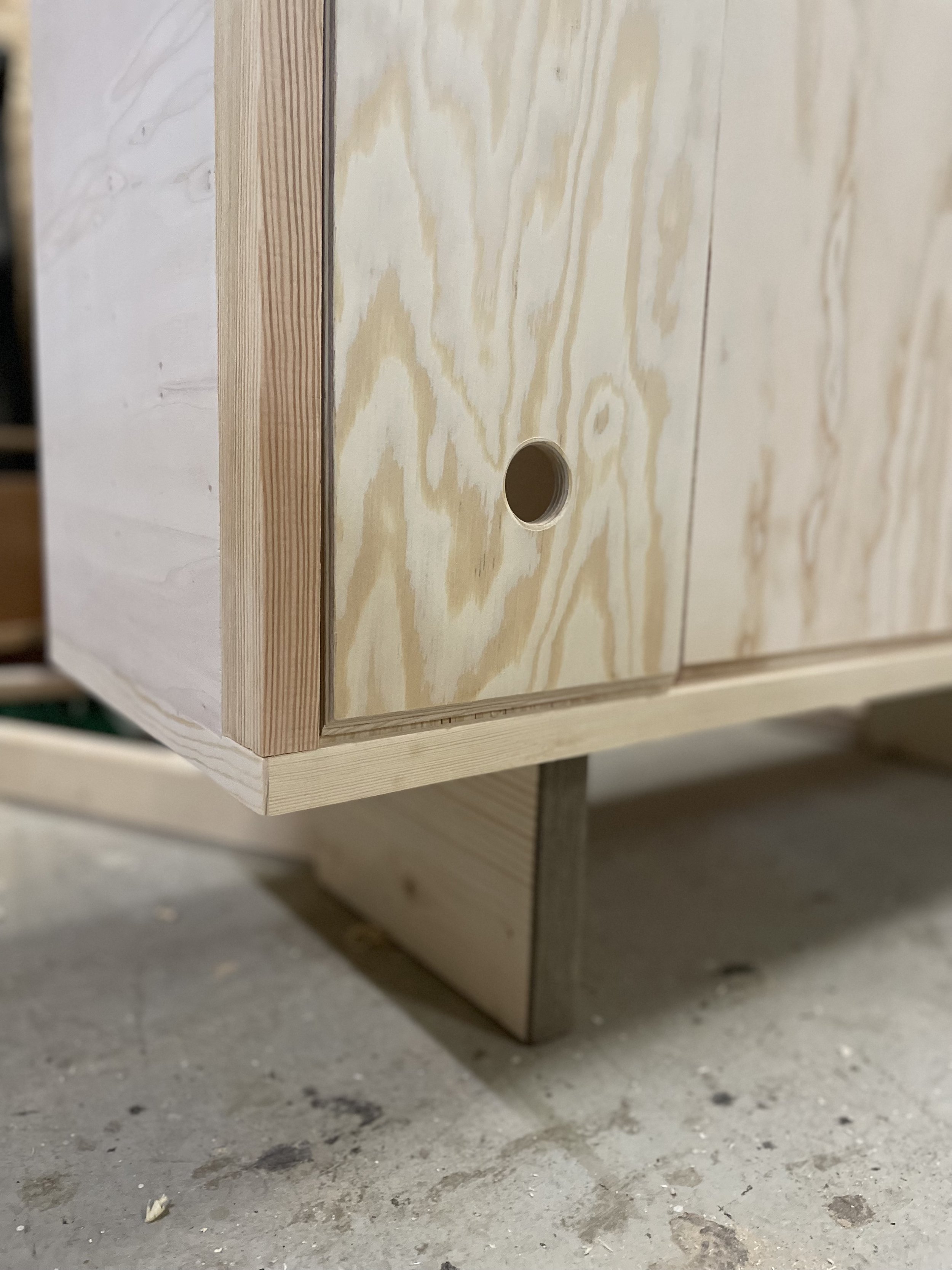 Holzmöbel mit runder Aussparung, in der Nähe eines Holzrahmens, auf einem Betonsockel aufgestellt.