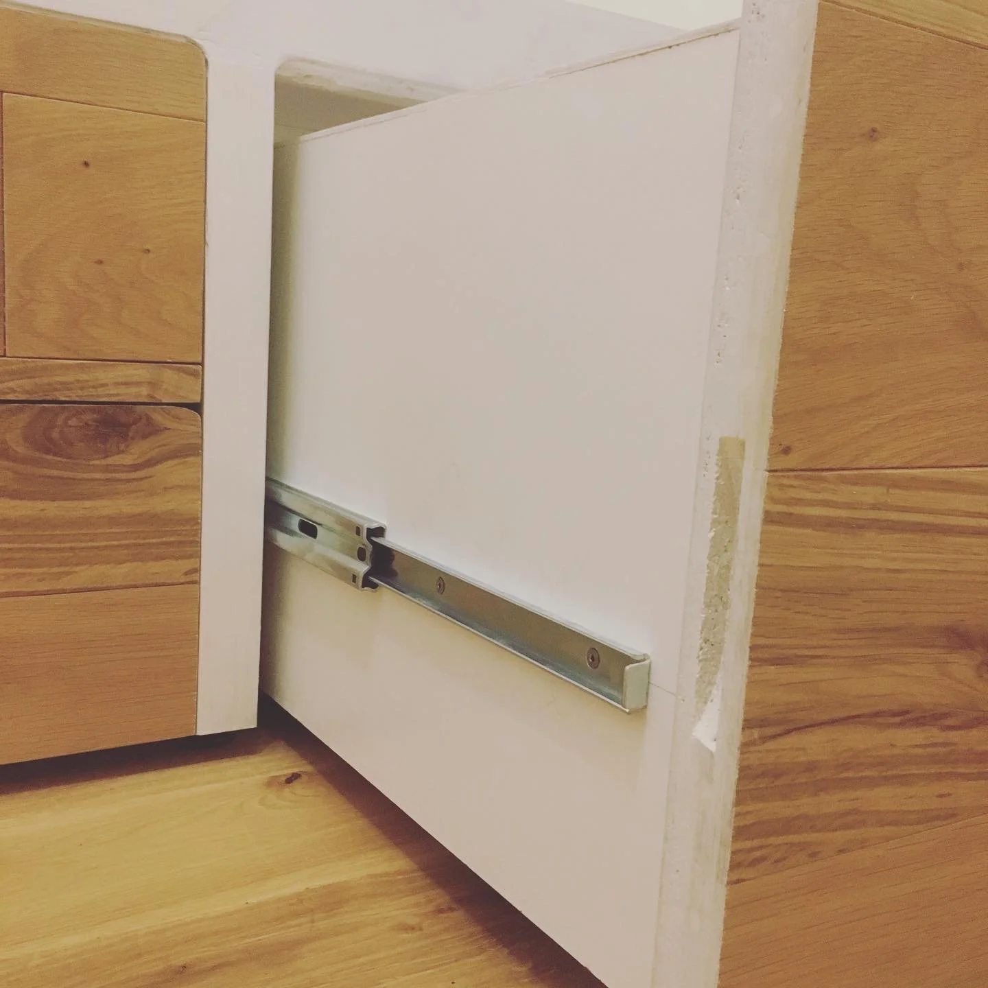 Unlackierte Küchenschublade mit Metallführung, eingebaut in Unterkonstruktion, zwischen Holzschränken