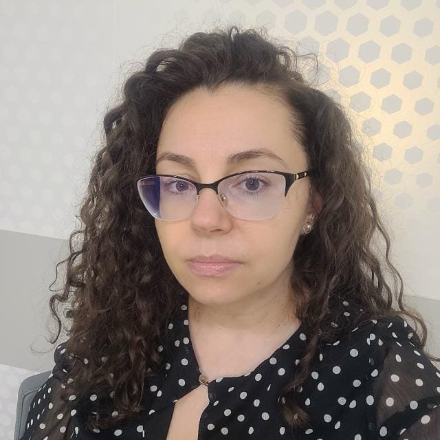 Woman with curly hair and glasses, wearing a polka dot blouse.