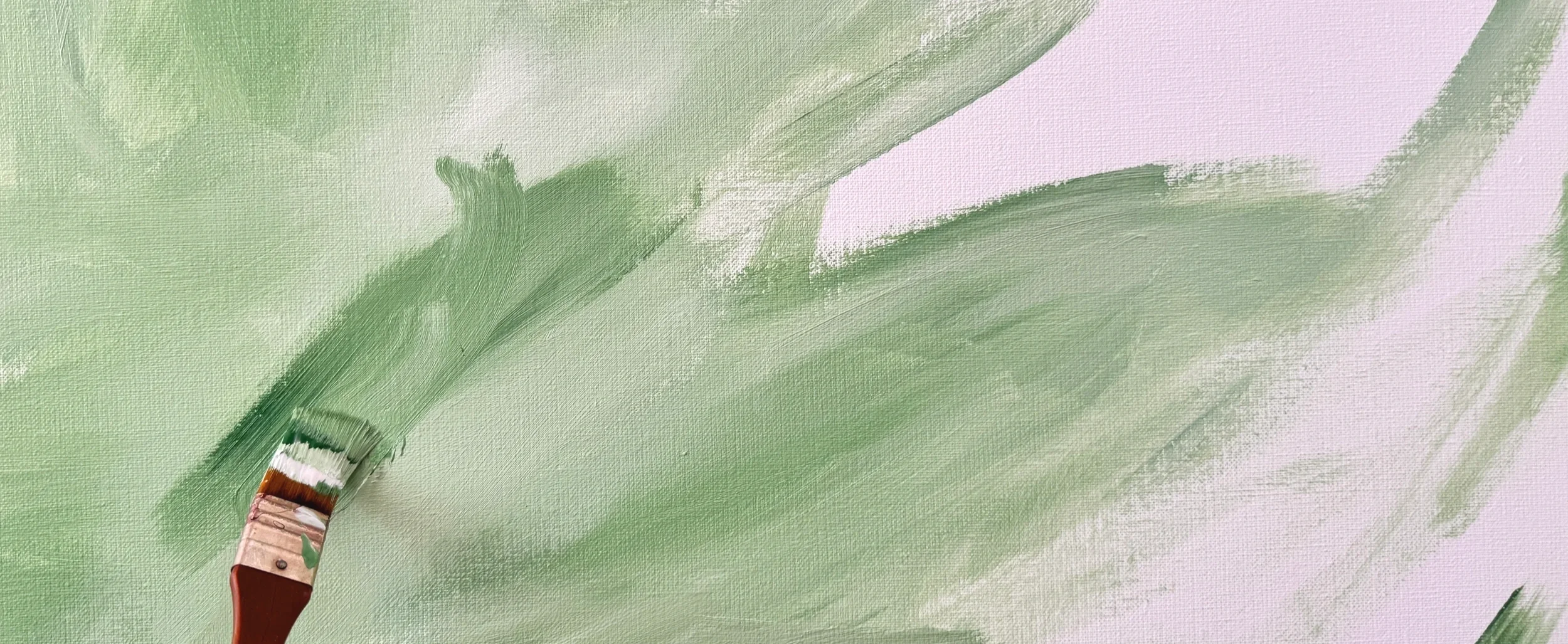 Close-up of a paintbrush applying light green paint on a canvas.