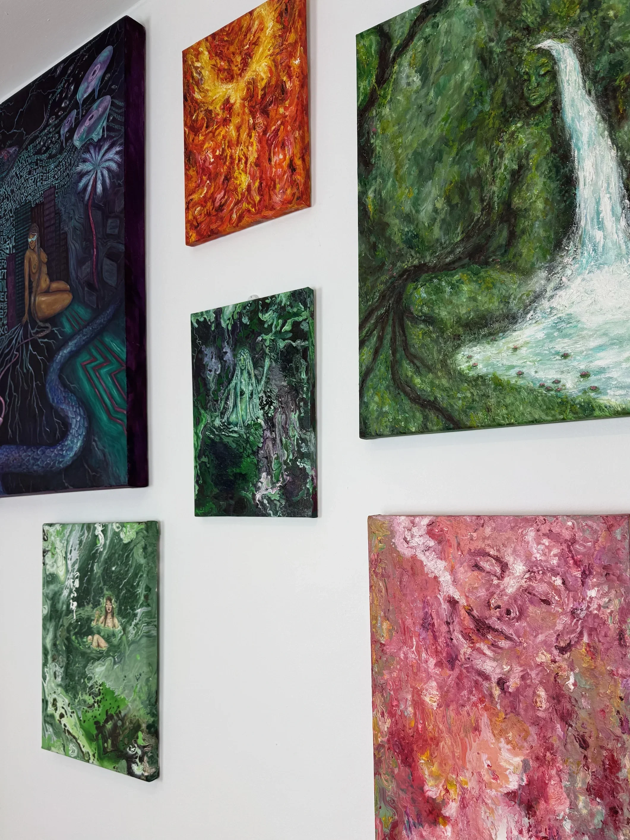 Various colorful abstract paintings on a white gallery wall, including one with a waterfall scene, one with fiery reds and oranges, another with green jungle imagery, and others with swirling patterns and human figures.
