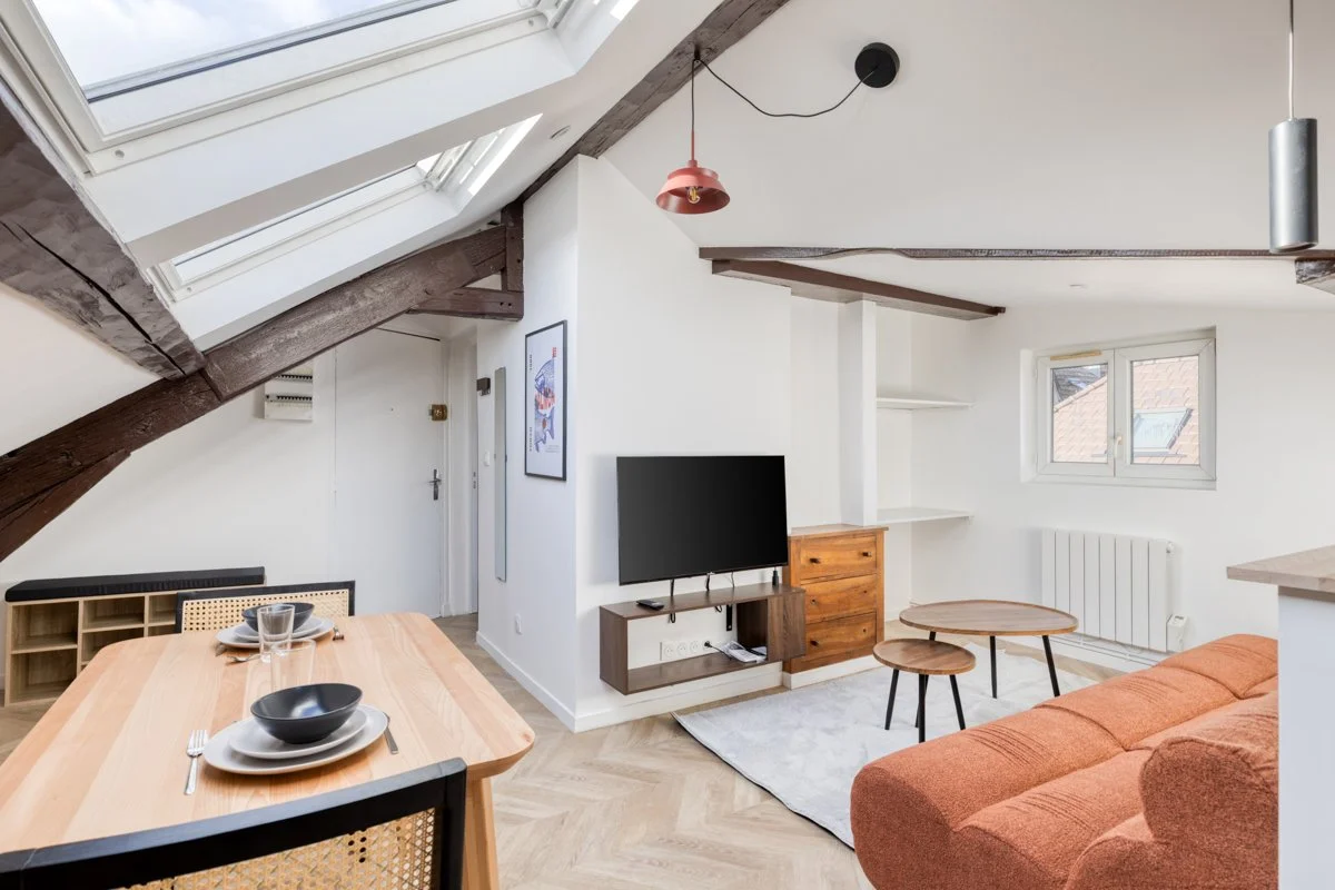 Salon de style moderne avec canapé orange, tableau sur le mur, télévison, fenêtres sous le toit et tables basses en bois