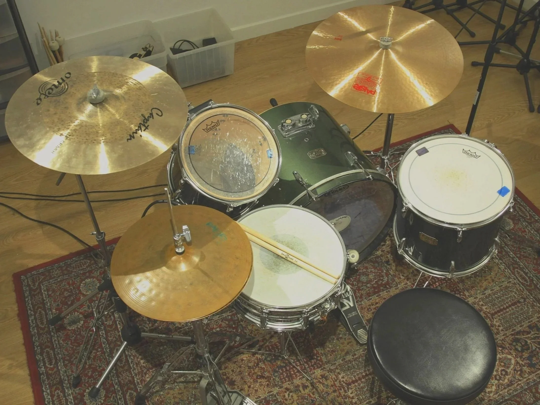 A drum set with three cymbals, a bass drum, snare drum, and tom-tom drums on a red patterned rug in a music room.