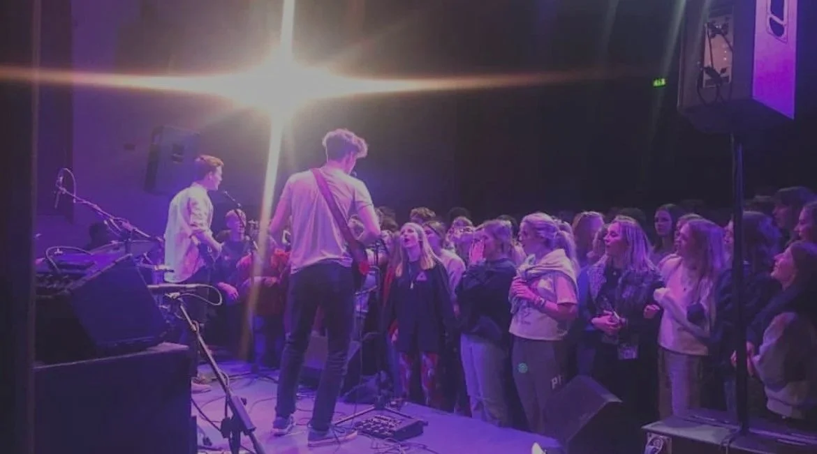 A band performing on stage with a crowd of young people watching.