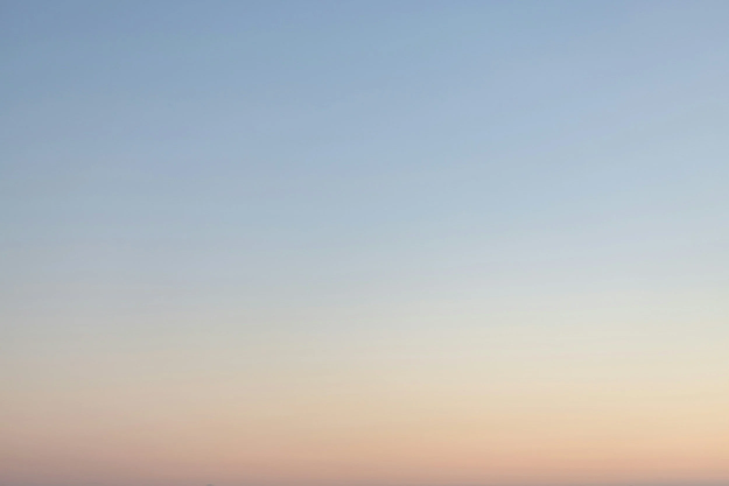 A colorful blurred view of a sky during sunrise or sunset with pastel hues of blue, pink, and orange.