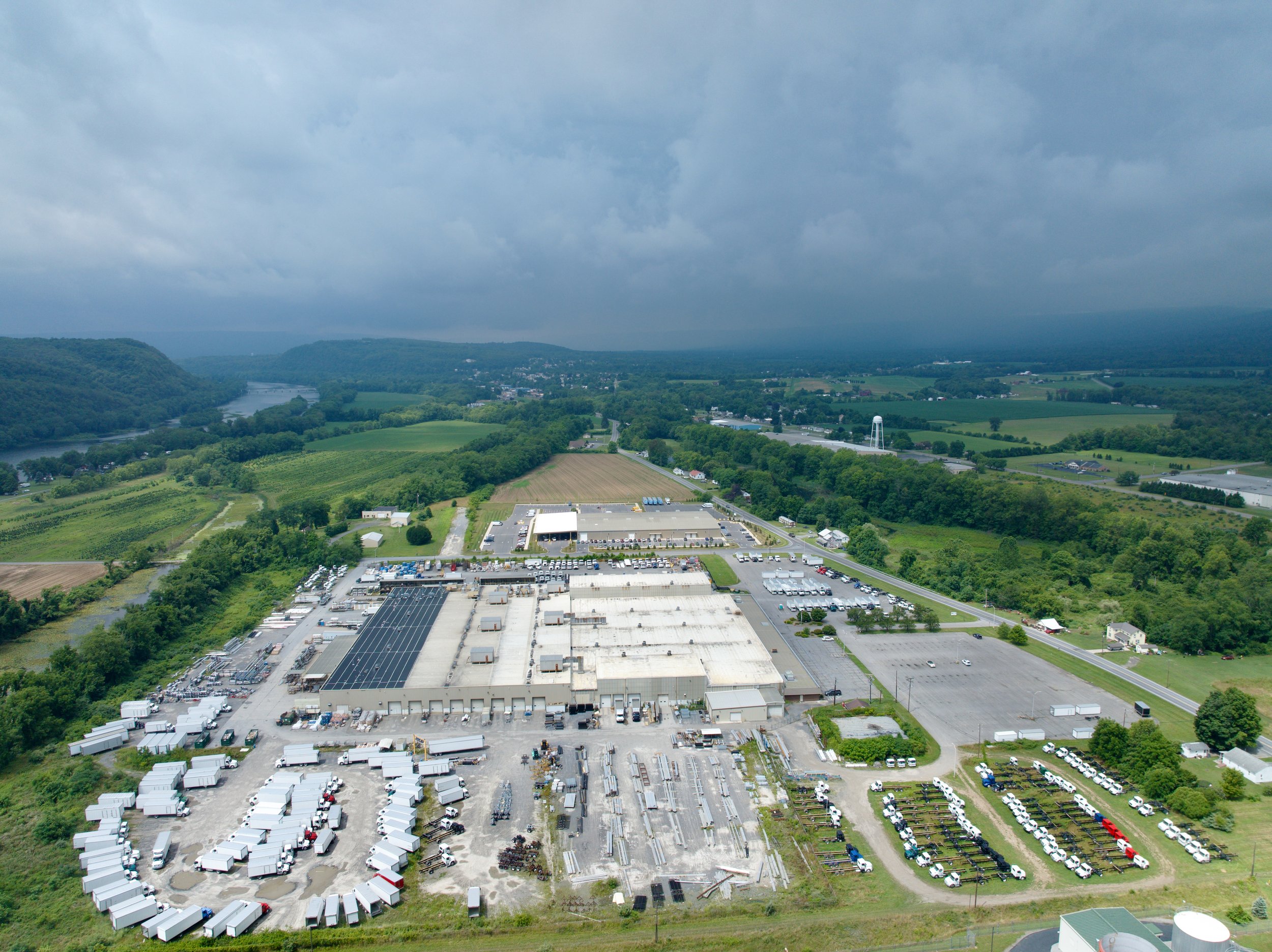 Aerial view of a large industrial complex surrounded by green fields and hills.