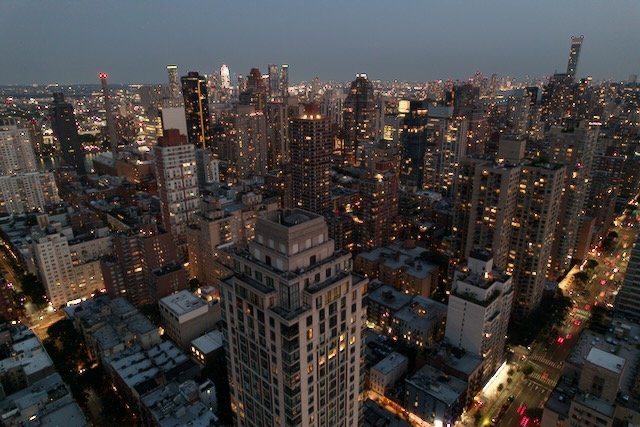 Aerial view of a city skyline with tall buildings at dusk, featuring illuminated skyscrapers and urban streets.
