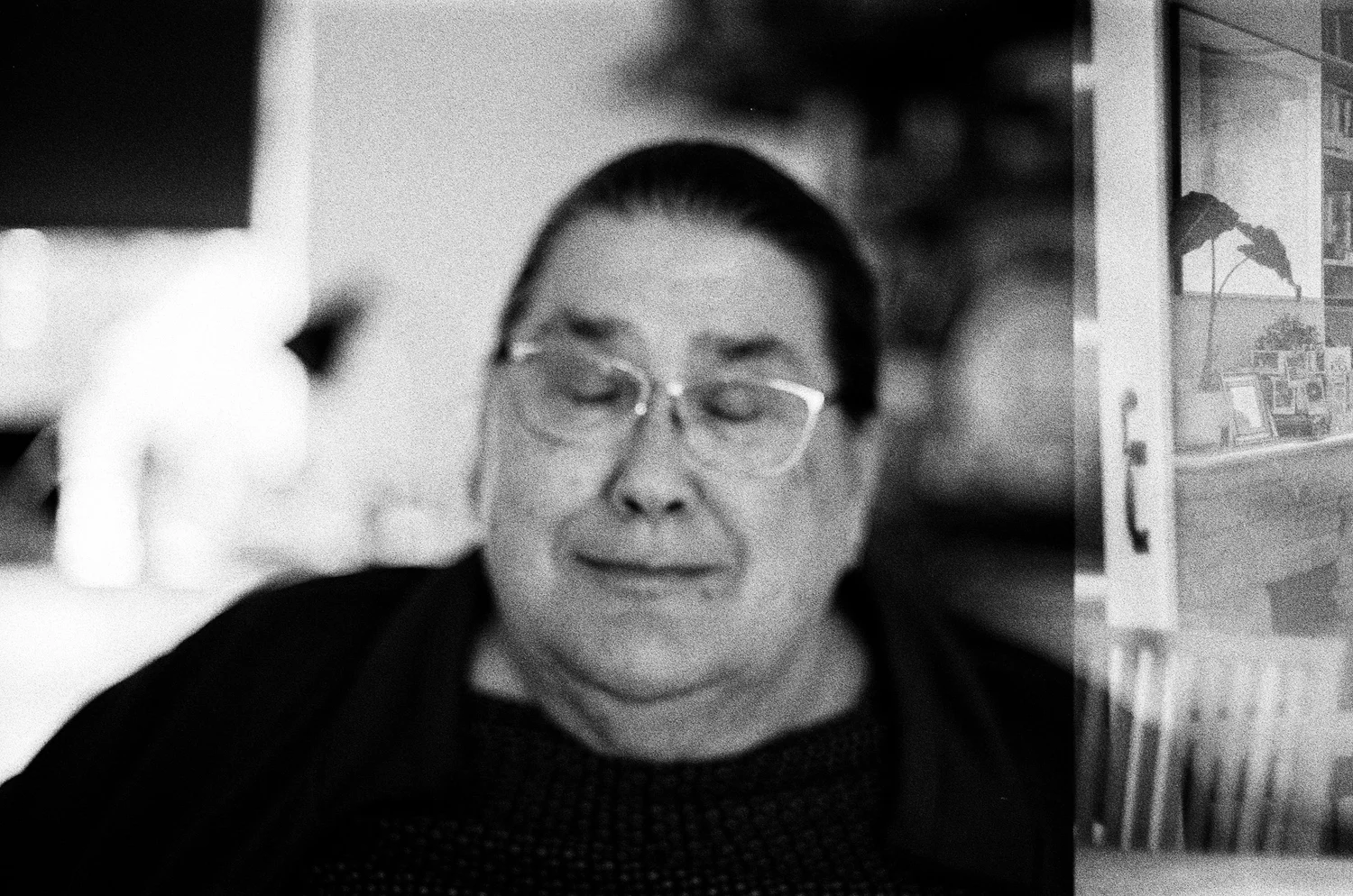 An elderly woman with glasses, eyes closed, smiling softly.