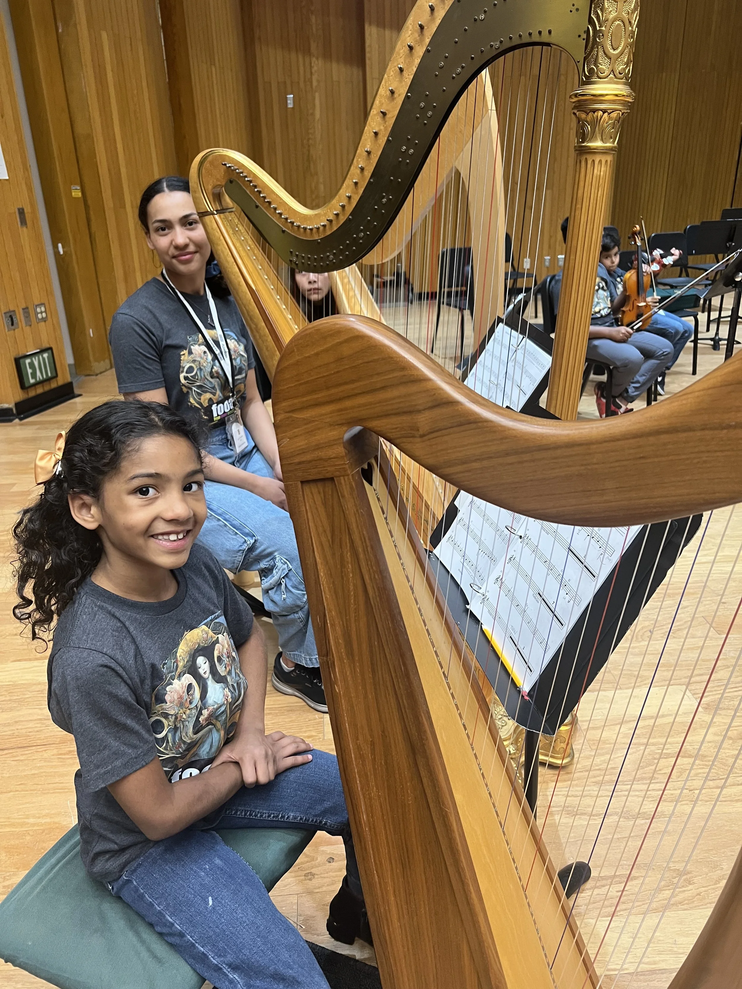 A smiling young girl plays a harp, highlighting upcoming student auditions for the Youth Orchestras of Fresno