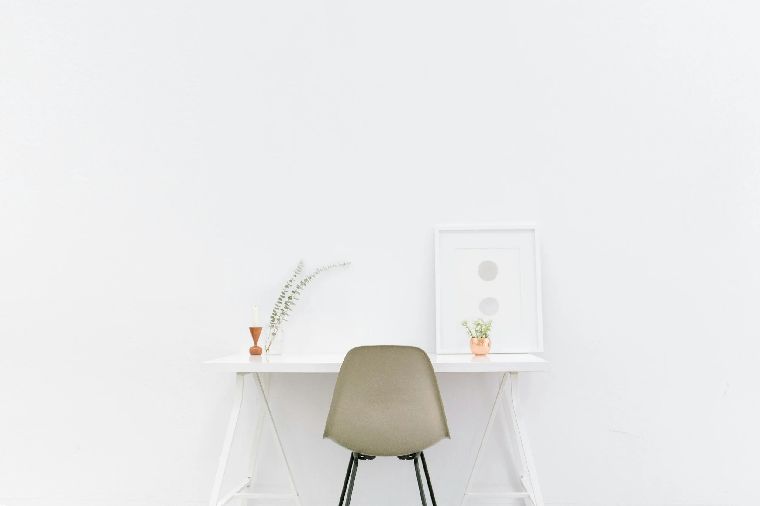 Minimalist white desk with a chair, framed art, candle, and plants.