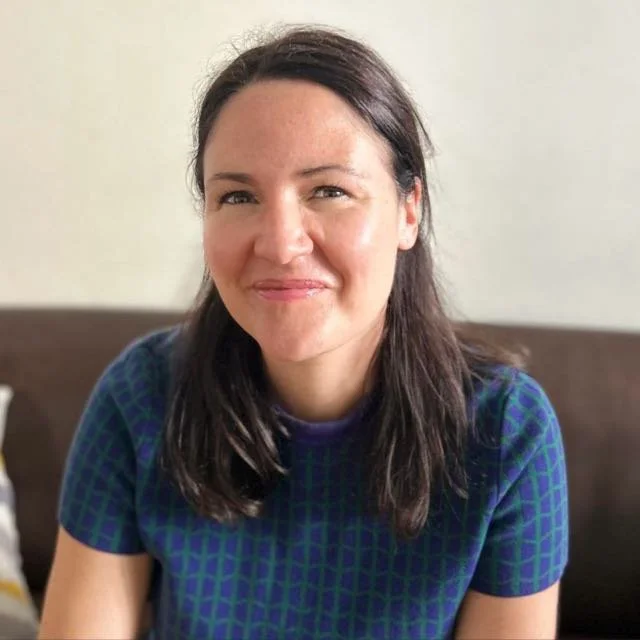 Heilpraktikerin für Psychotherapie mit dunklen Haaren, die lächelnd in die Kamera schaut, sitzend auf einem Sofa.