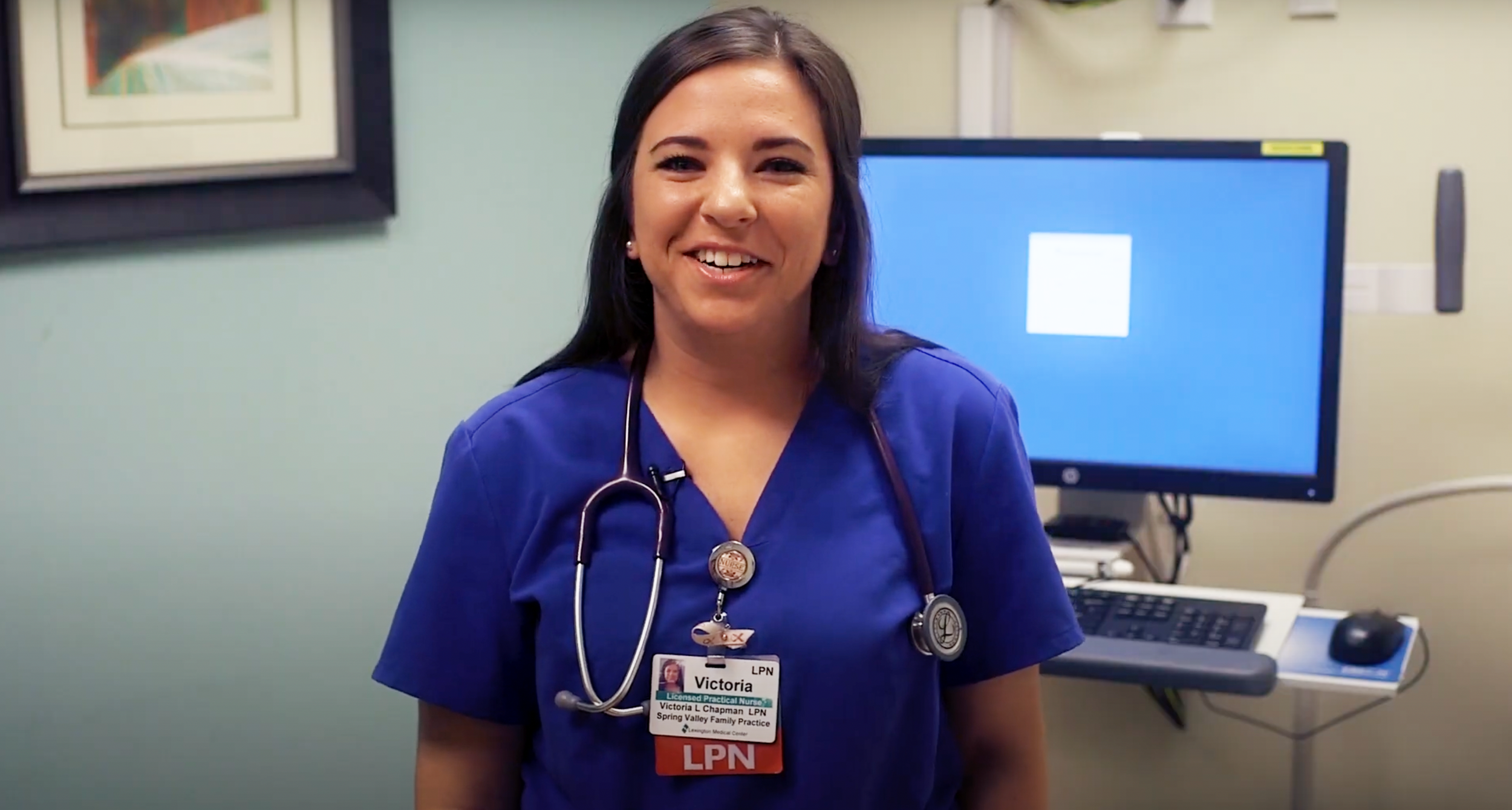 A smiling nurse in royal blue scrubs and a stethoscope around her neck.
