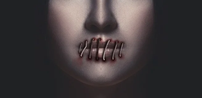 A face with red paint on their lips and multiple metal staples or pins crossing over the mouth, giving a dark and unsettling appearance.