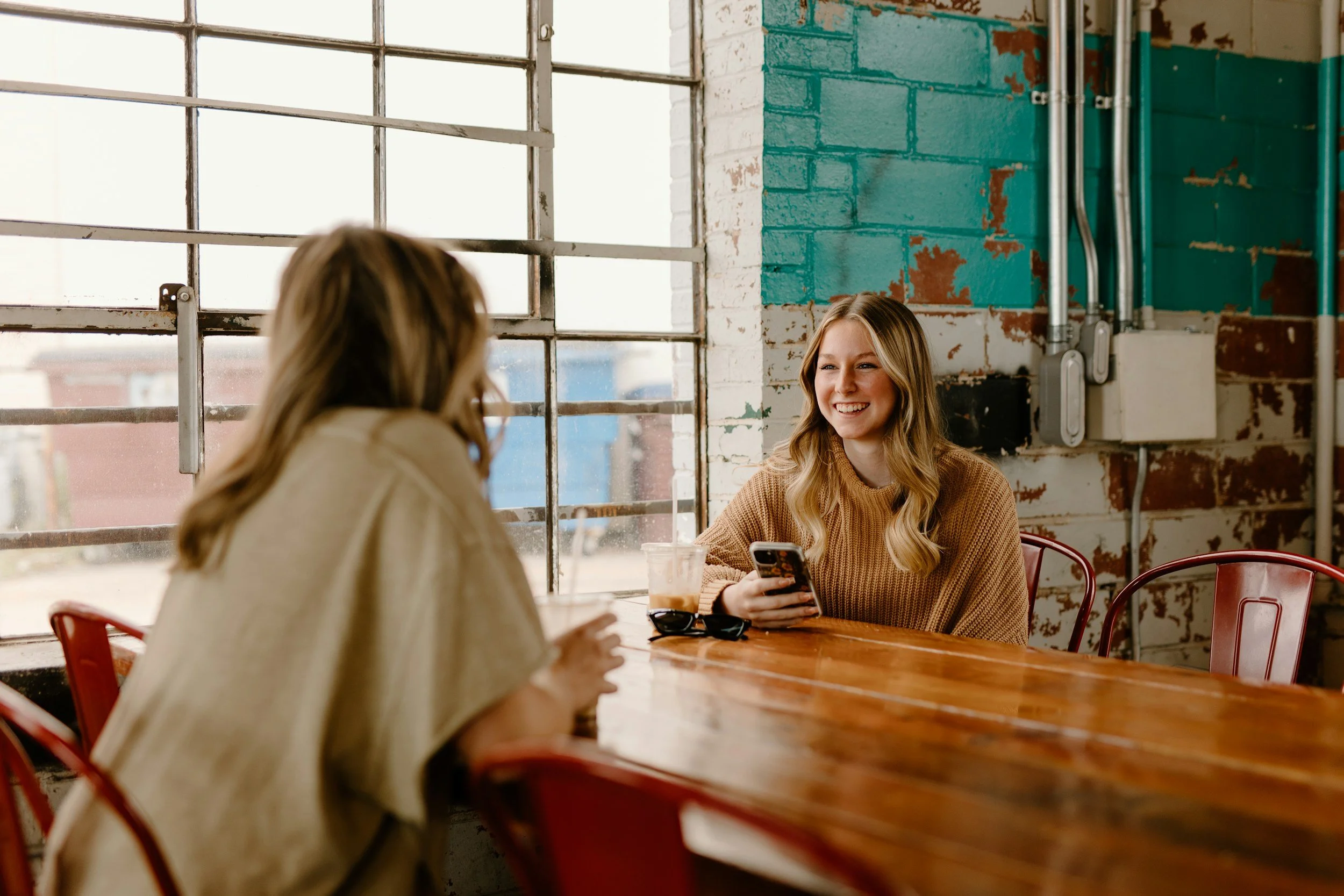 Two white women sit across from one another in a coffee shop