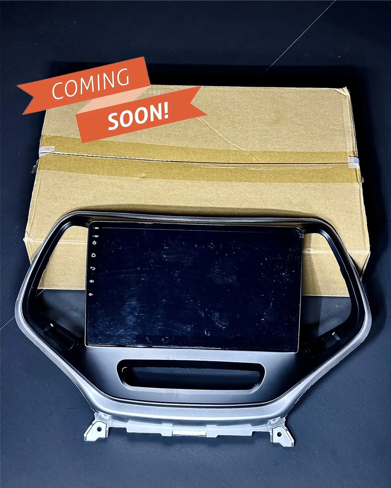 Dashboard display screen with frame on a cardboard box, "COMING SOON" banner.