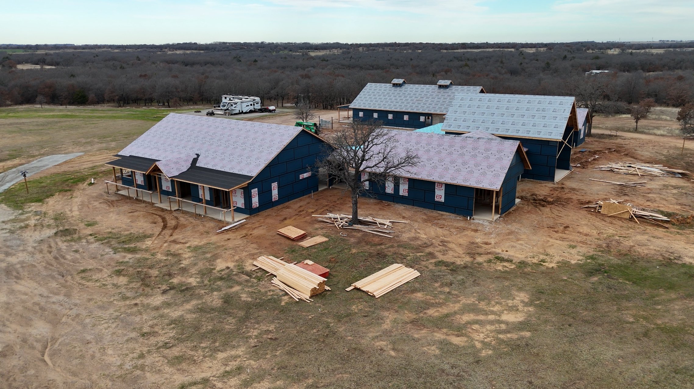 A bird’s-eye view of The Essex Ranch construction site, showcasing the framed structures of the guest house, garage, and main house. The crisp lines of progress against the backdrop of open fields reflect the ranch’s promising future.