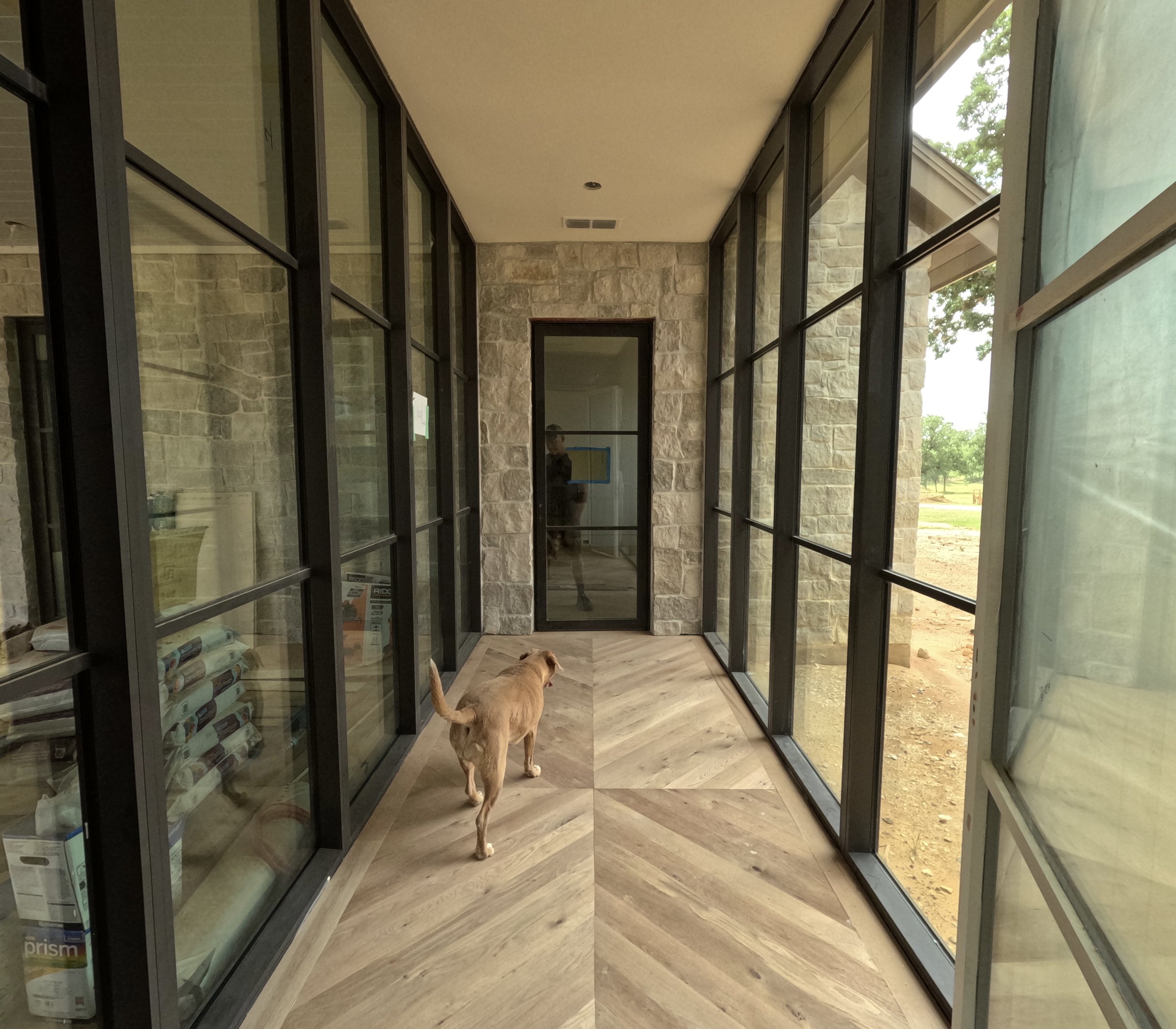 One of two glass corridors connecting the home’s living spaces, featuring herringbone flooring and stone accents.