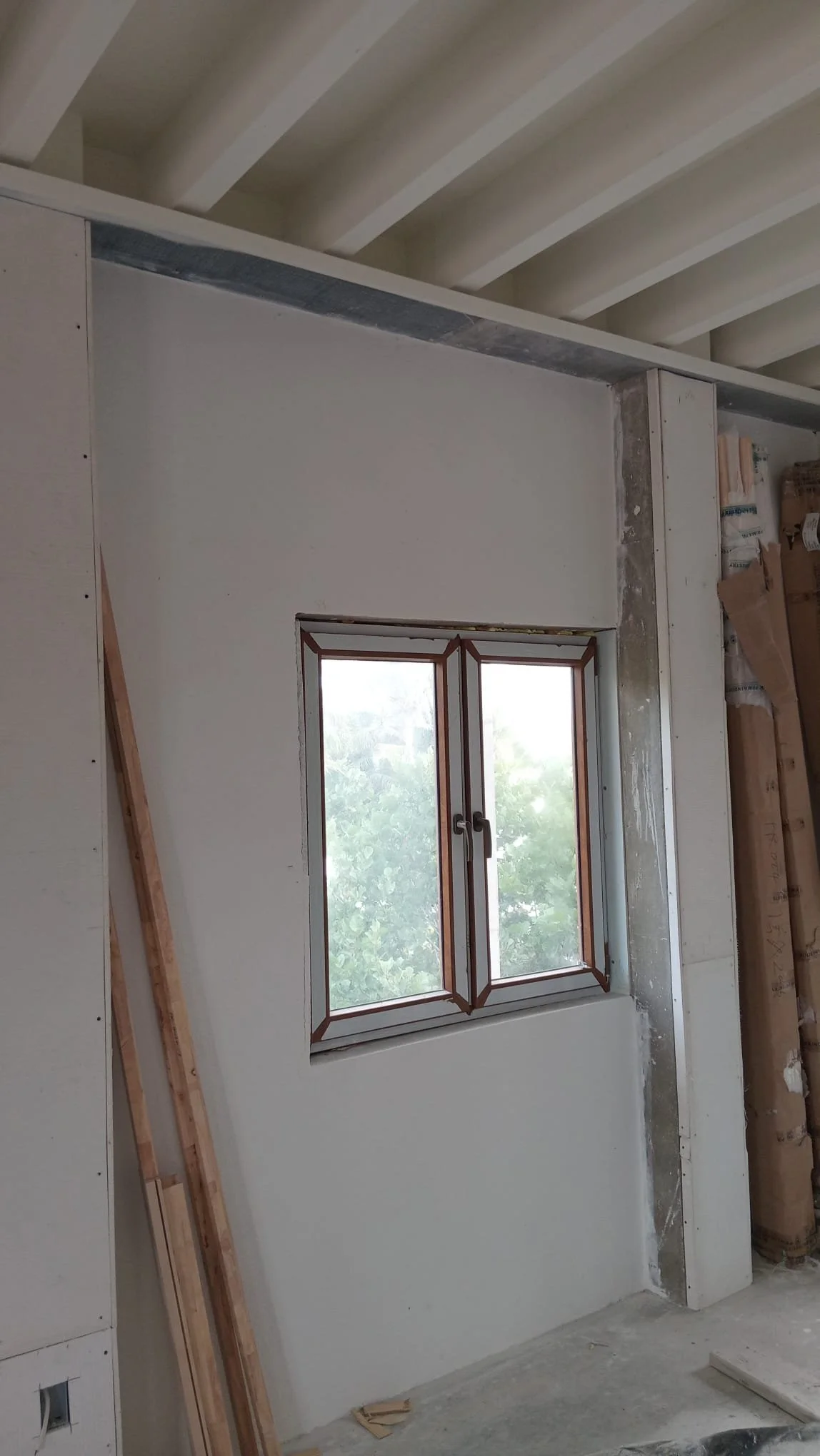 Interior view of a room under construction with a window, drywall, and construction materials.