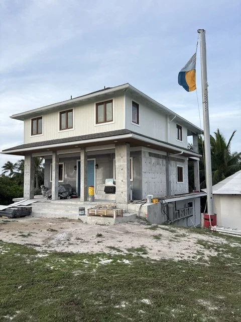 A two-story house under construction with a flagpole and a partially finished exterior.