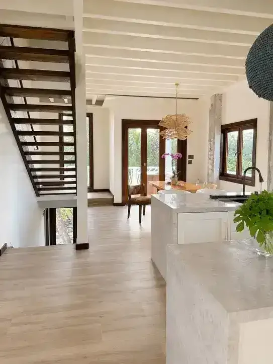 Modern open-concept kitchen and dining area with large windows, a wooden dining table, and a staircase leading upstairs.