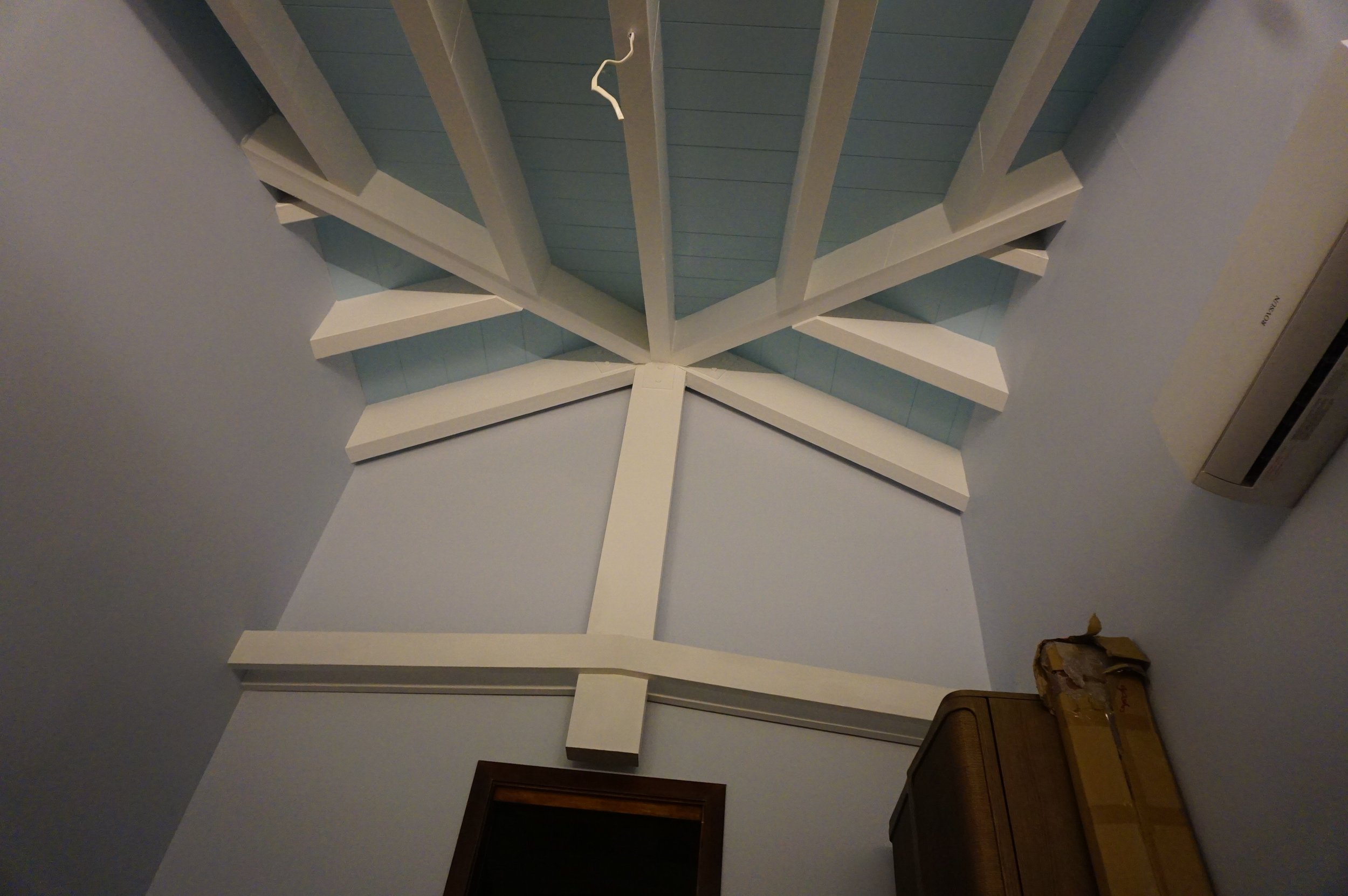 Ceiling with wooden beams painted white and blue, and a wall-mounted air conditioning unit in the corner.