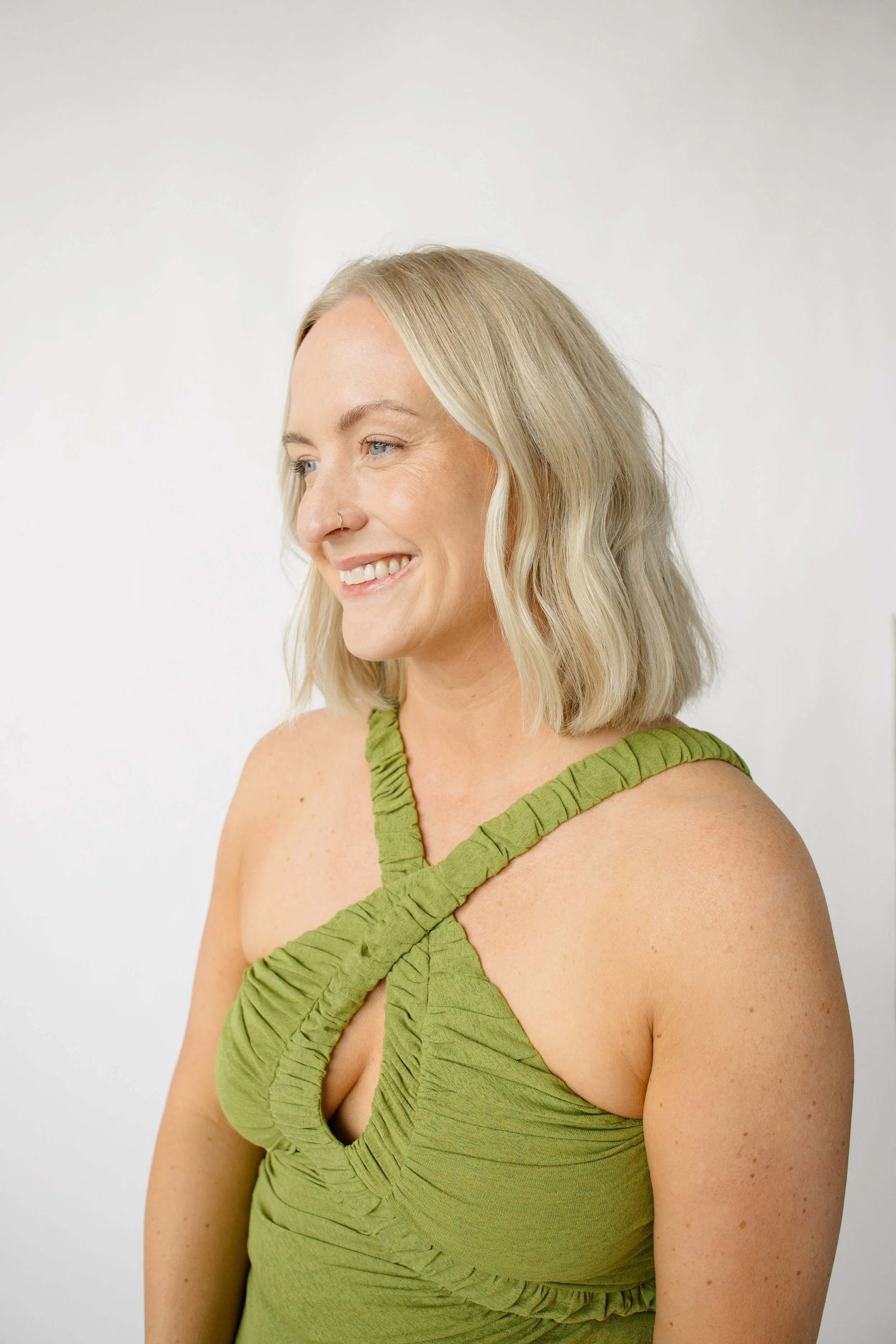 A woman in a black athletic outfit leaning against a white wall with one hand, with tattooed Roman numerals on her left forearm and gold jewelry.