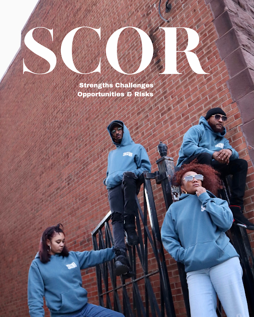 Four young people wearing blue hoodies with the SCOR logo posing against a brick wall, with two sitting on a railing and two standing, one leaning on the railing and one sitting at the top.
