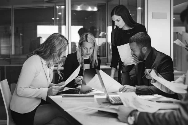 Group of five professionals working together in a modern office, reviewing documents and a laptop.