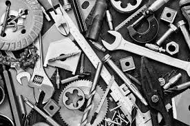 A cluttered collection of various hand tools and mechanical parts, including wrenches, screwdrivers, gears, and bolts, in black and white.