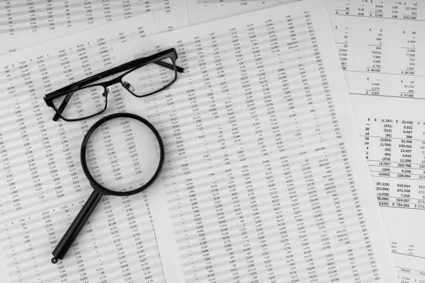 Financial documents with a pair of black glasses and a magnifying glass on top.