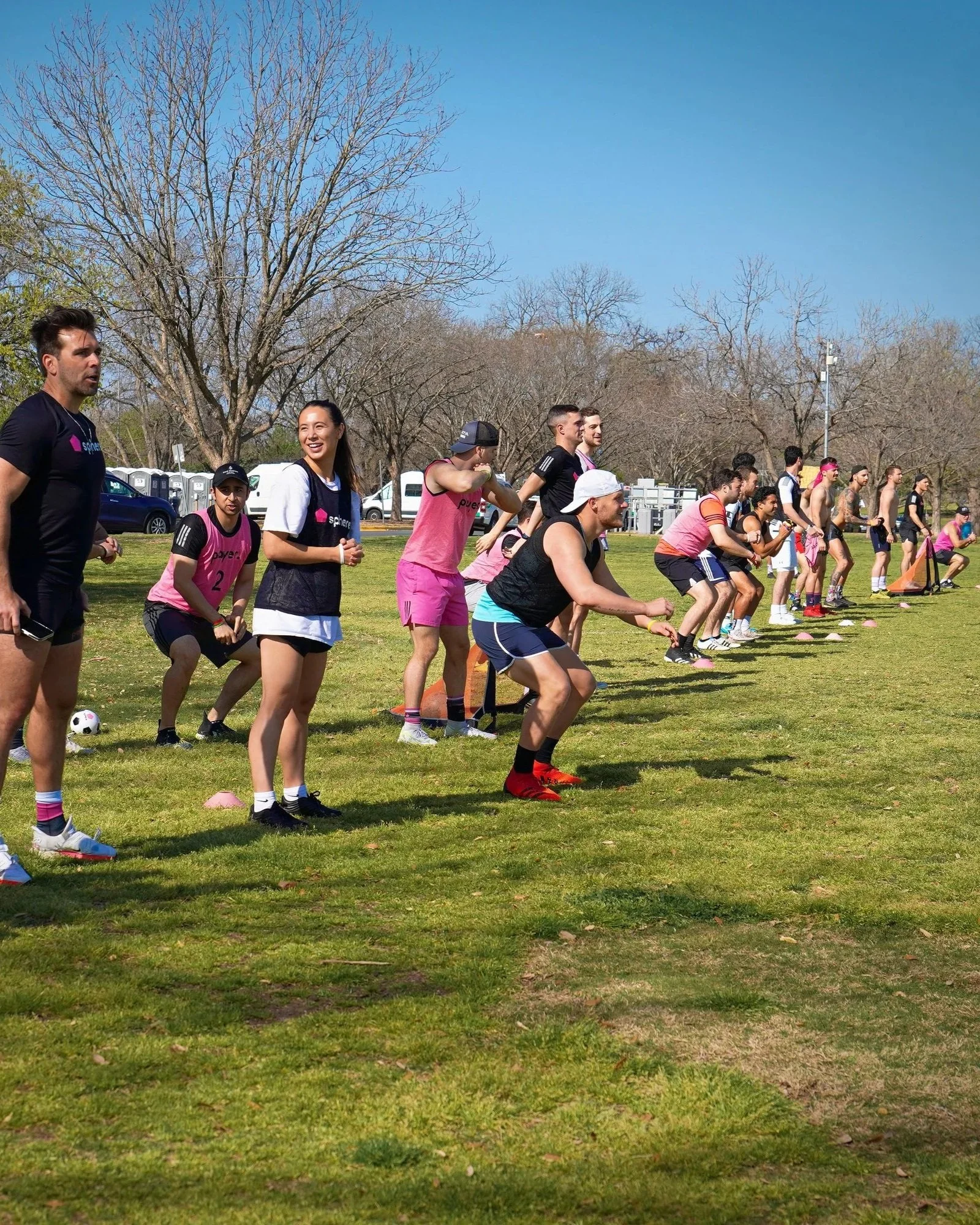 sphere™ Group of men and women in sports attire playing a game outdoors, wearing pink pinnies, with trees in the background.
