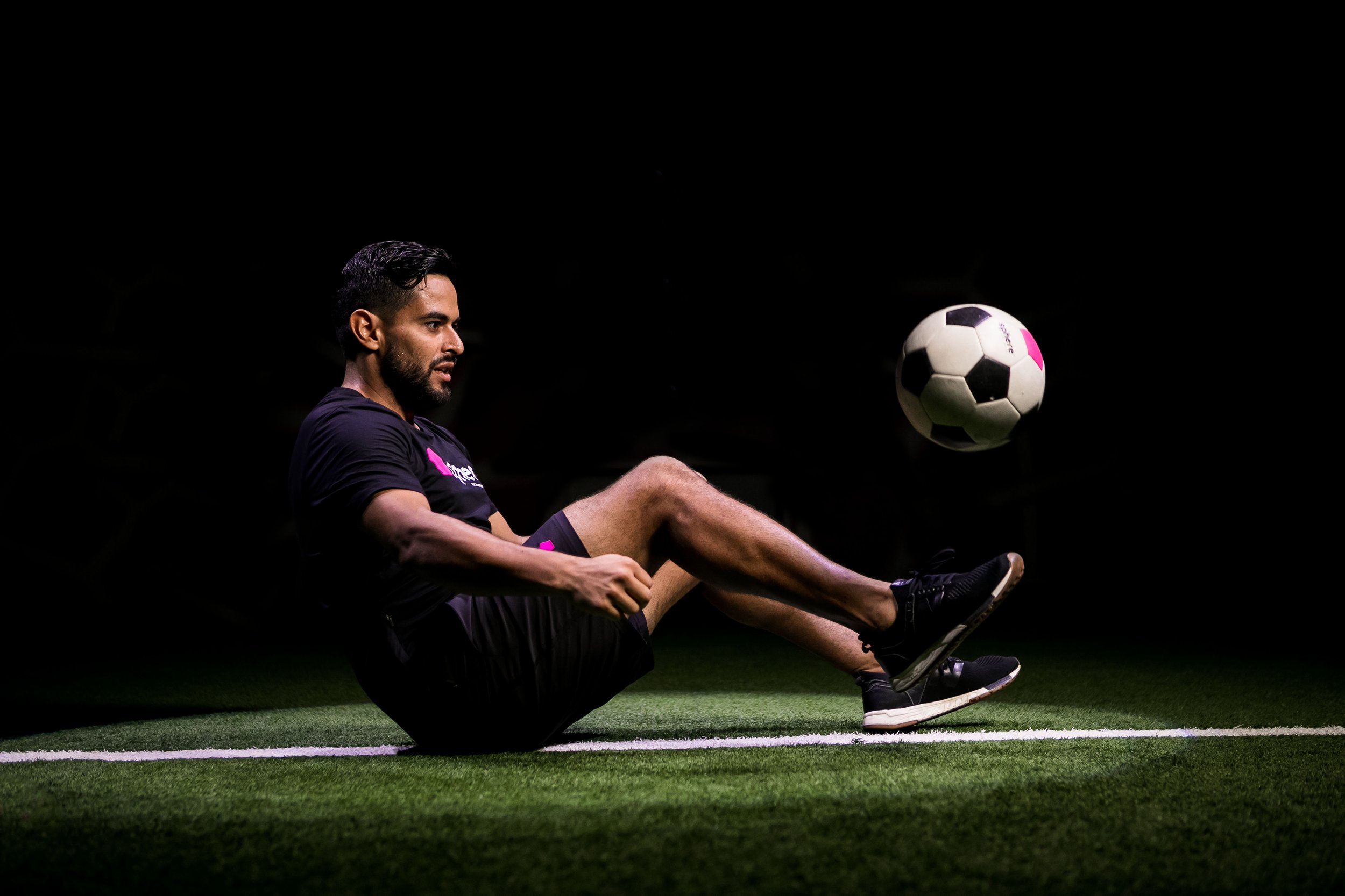 Two sphere™ players playing soccer outdoors, one wearing a pink tank top and the other in a black shirt, with a soccer ball on a grassy field.