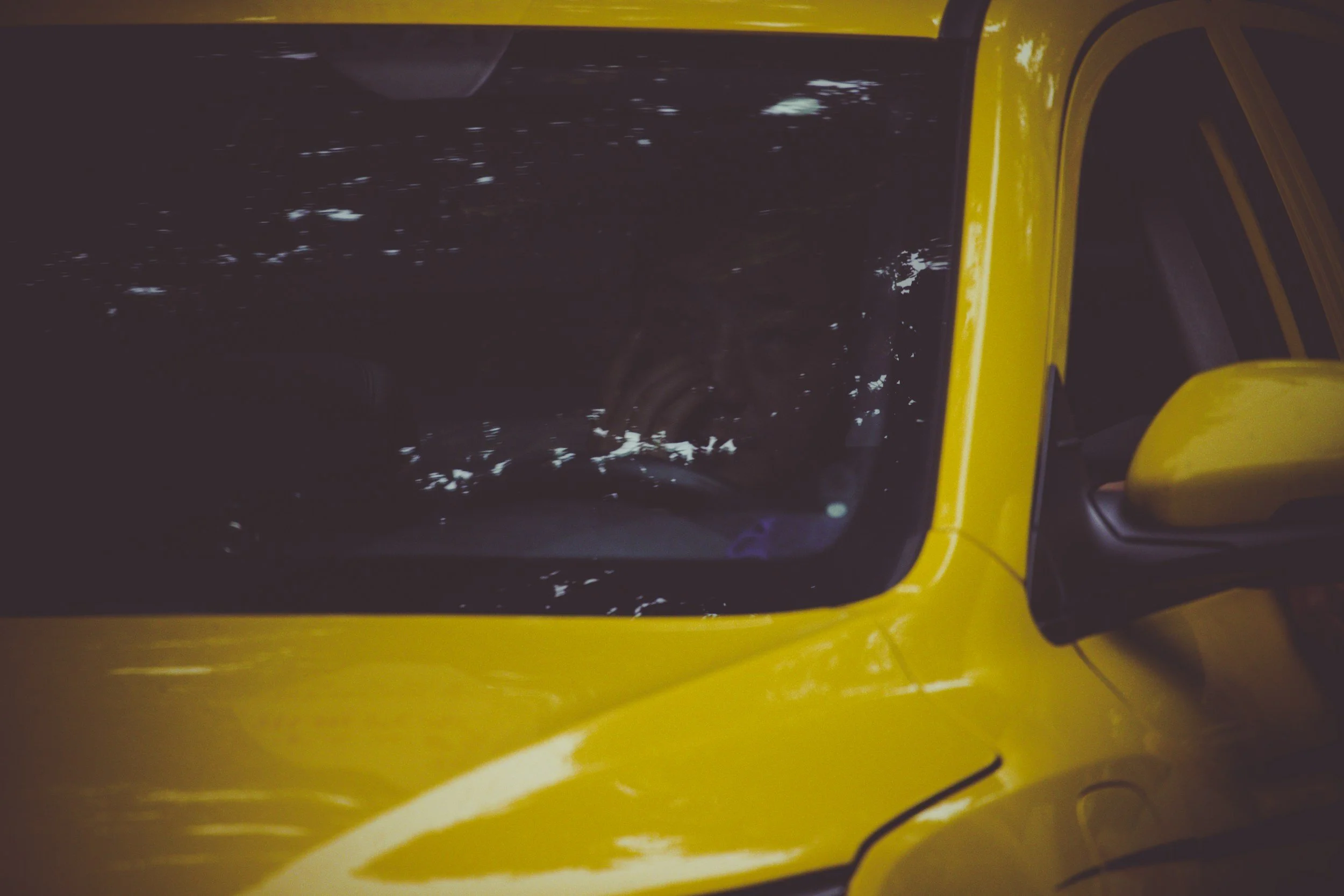 Close-up of a yellow vehicle, showing its black windshield with reflections and a side mirror.