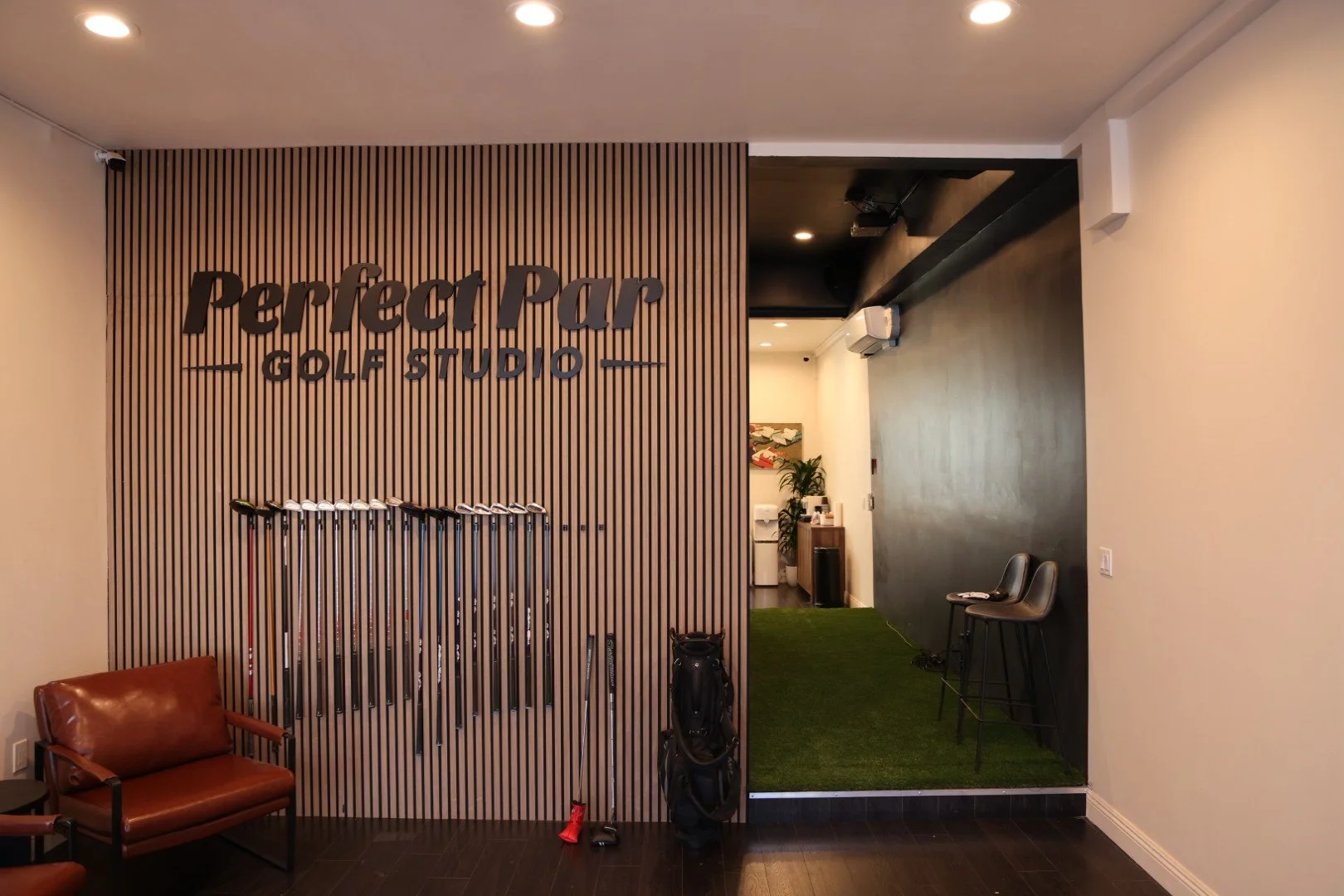 Golf studio interior with golf clubs, chairs, artificial turf, and "Perfect Par Golf Studio" signage, Koreatown Los Angeles LA