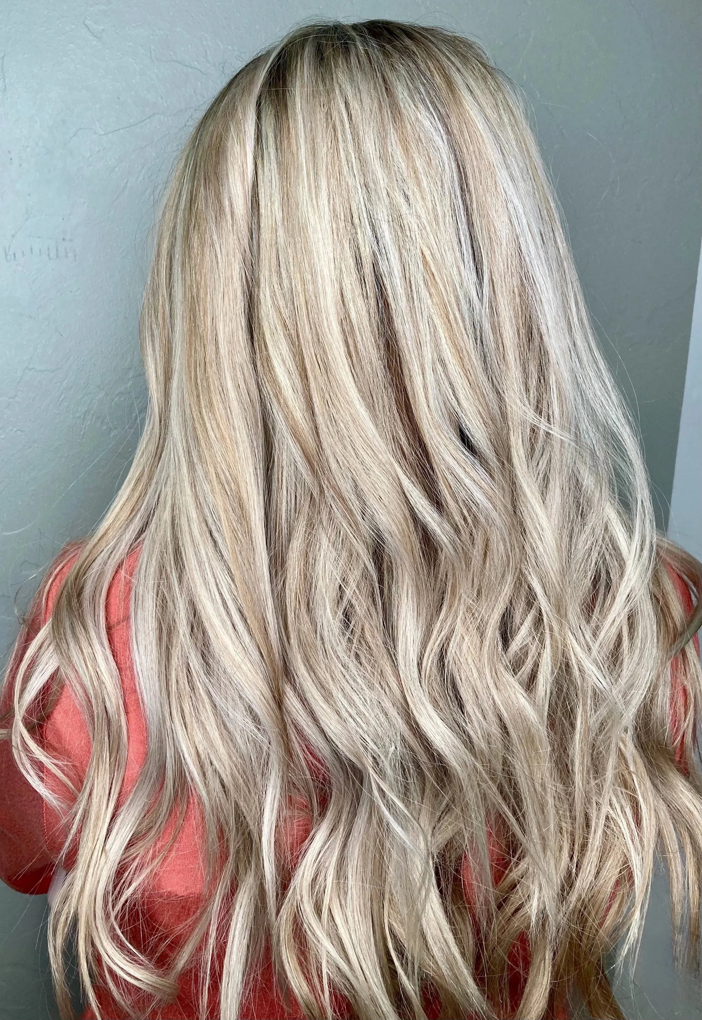Back of a person's head with long, wavy, blonde hair wearing a pink top.
