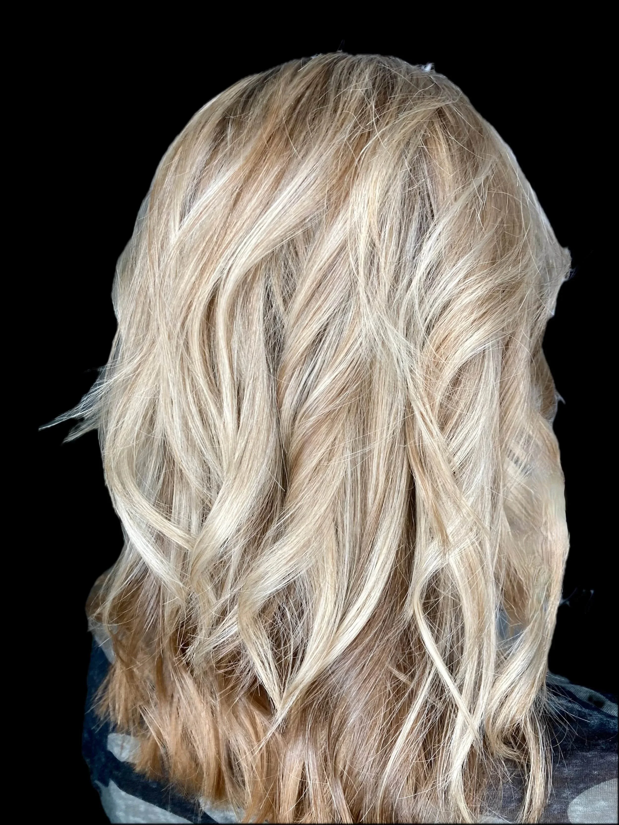 Blonde wavy hair hairstyle babylights on a person against a black background.