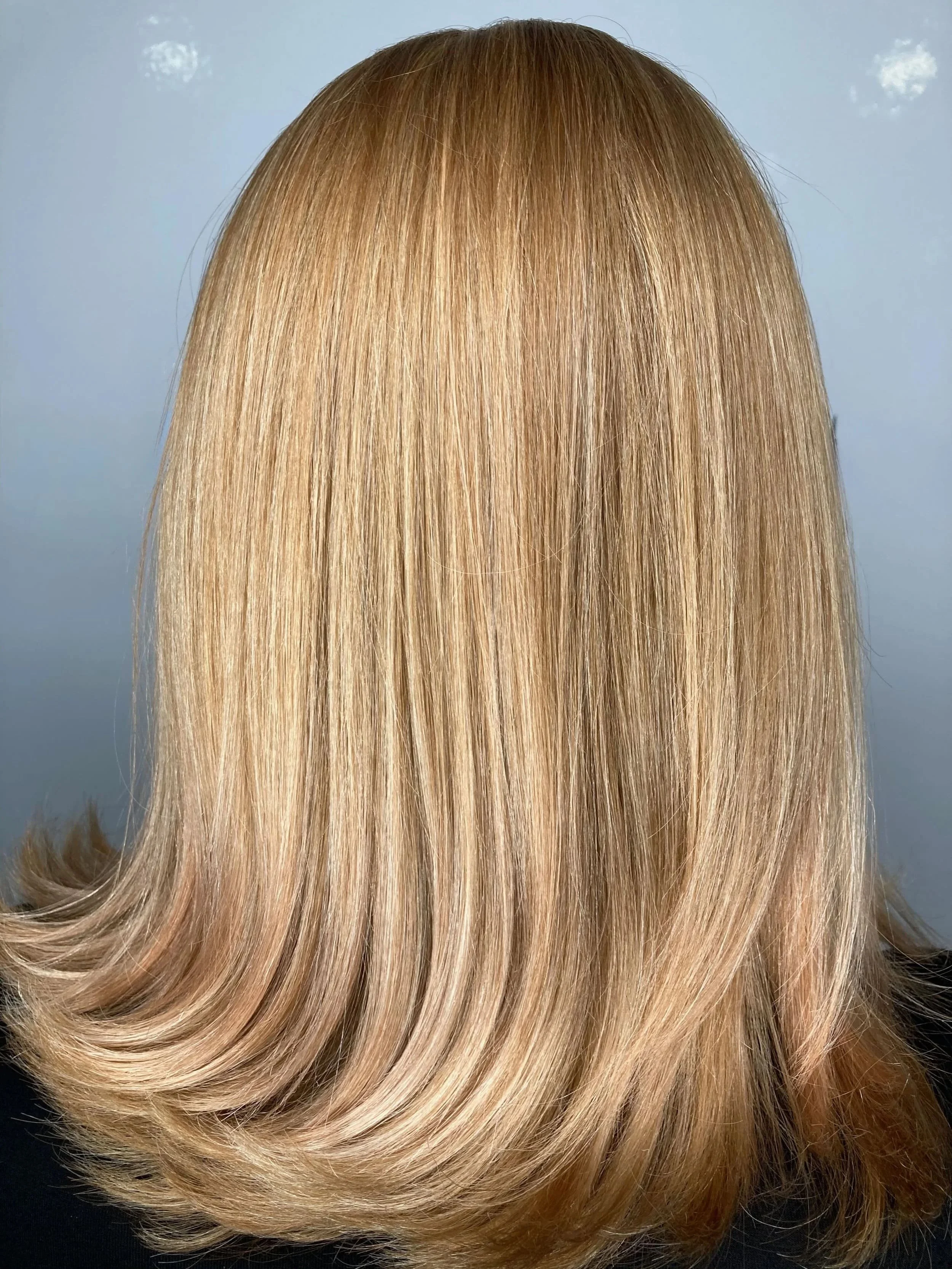 Back of a person's head with straight blonde hair that has soft layers and a slight outward curl at the ends.