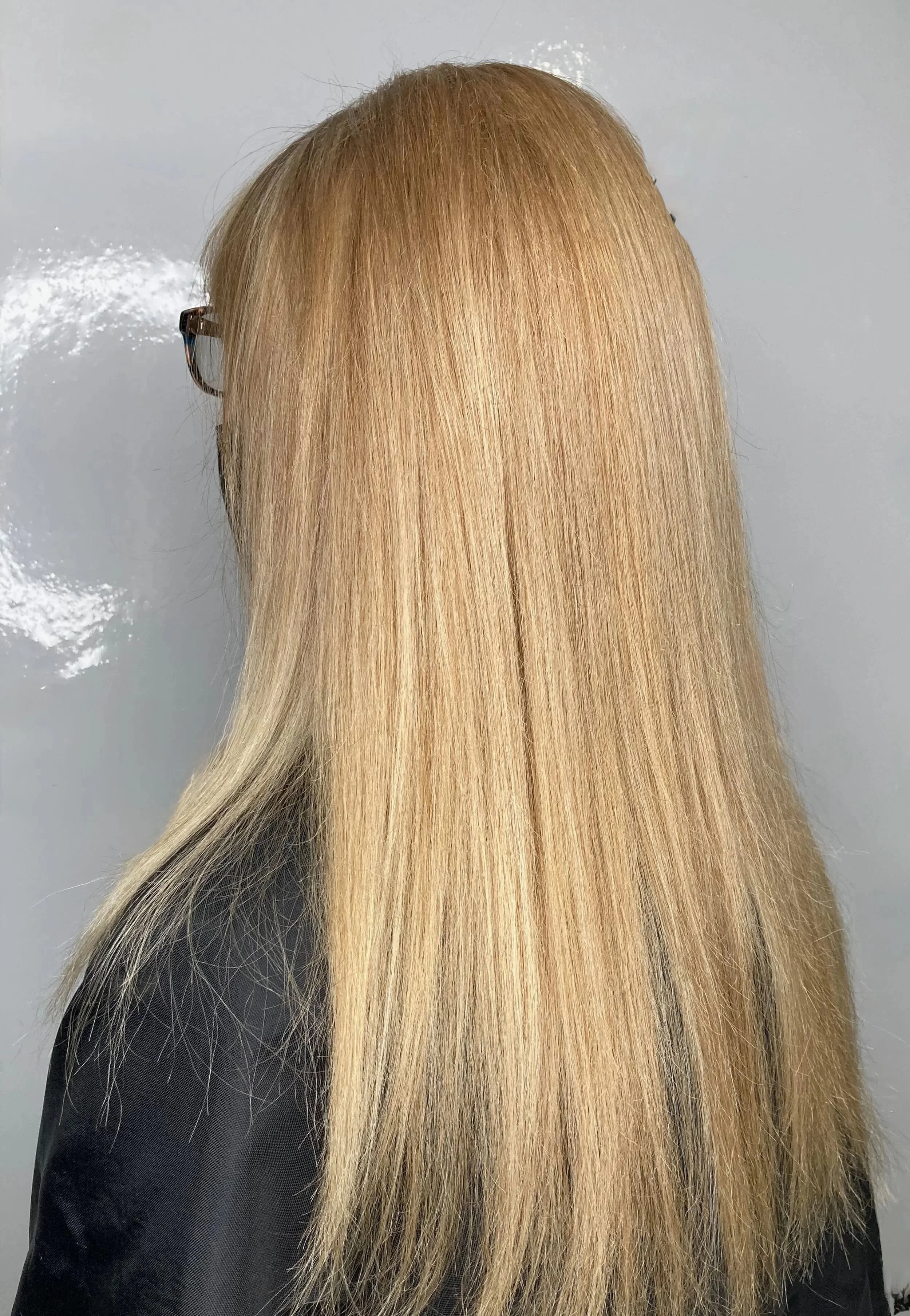 Back view of a woman with straight, long blonde hair wearing glasses and a black top.