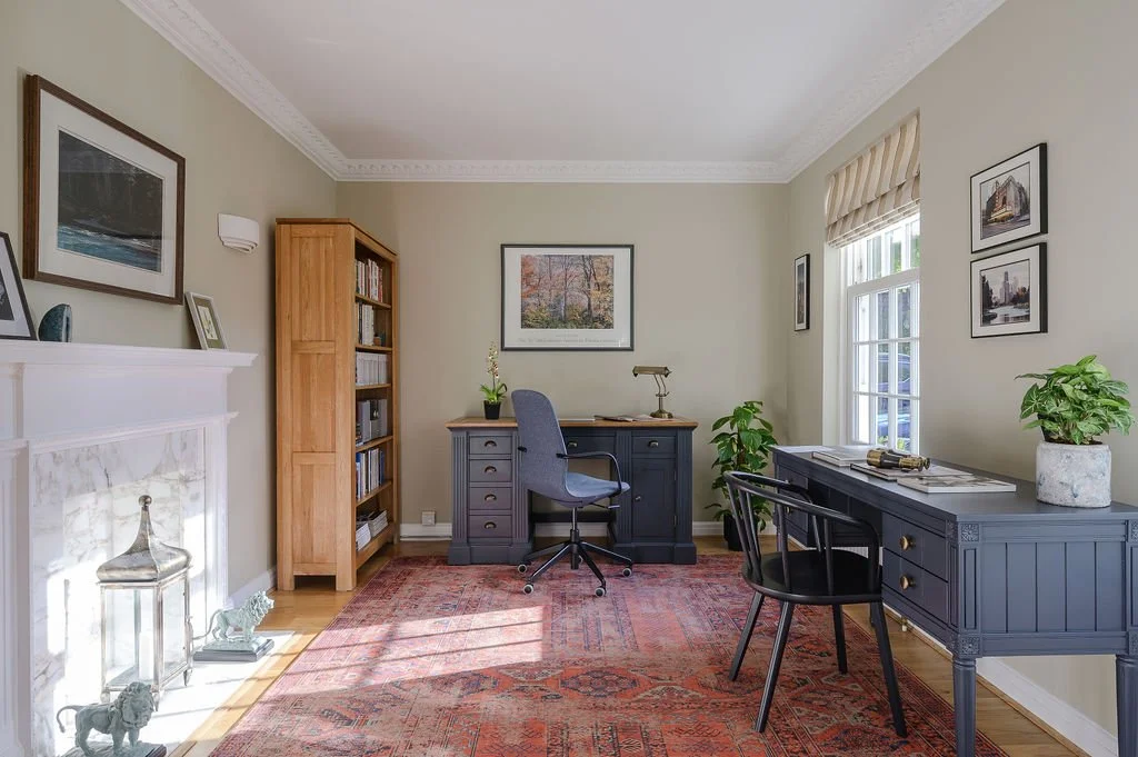 Home office designed by Laura Charlick, with two blue desks, black chairs, a grey office chair, potted plants, and framed artwork on light-coloured walls.