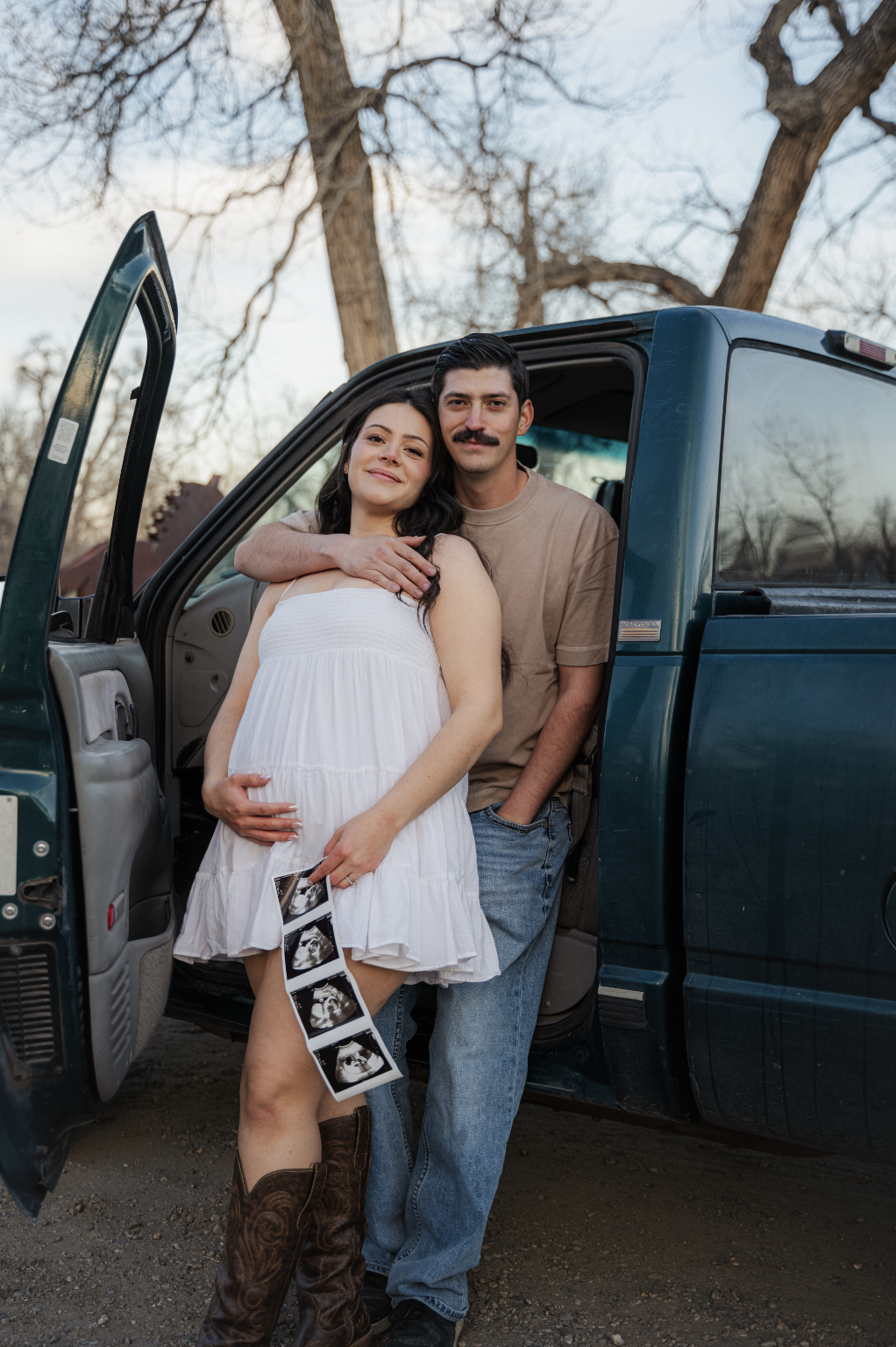 A couple standing in front of a blue pickup truck, giving a soft vintage country feel for a maternity photoshoot with maternity ultrasound images in Colorado. Shot by Maya Kirschenbaum | PhotosByMaya 