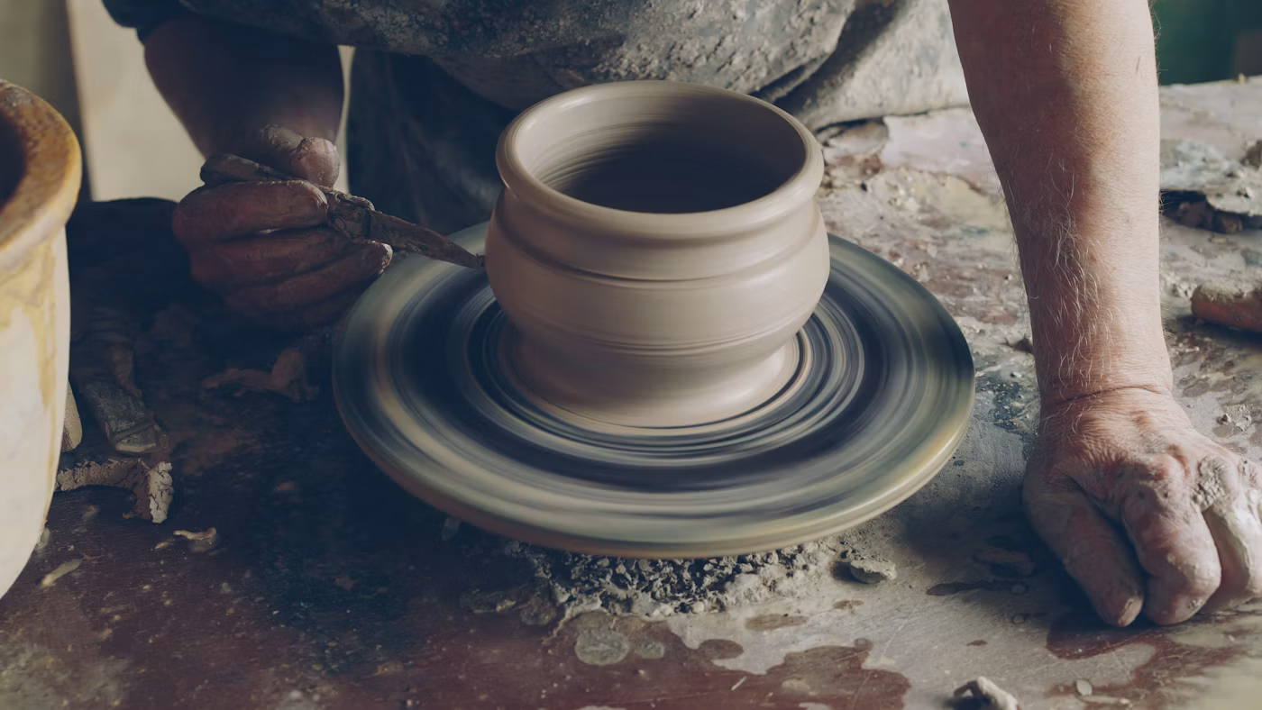 A person shaping a clay pot on a spinning pottery wheel.