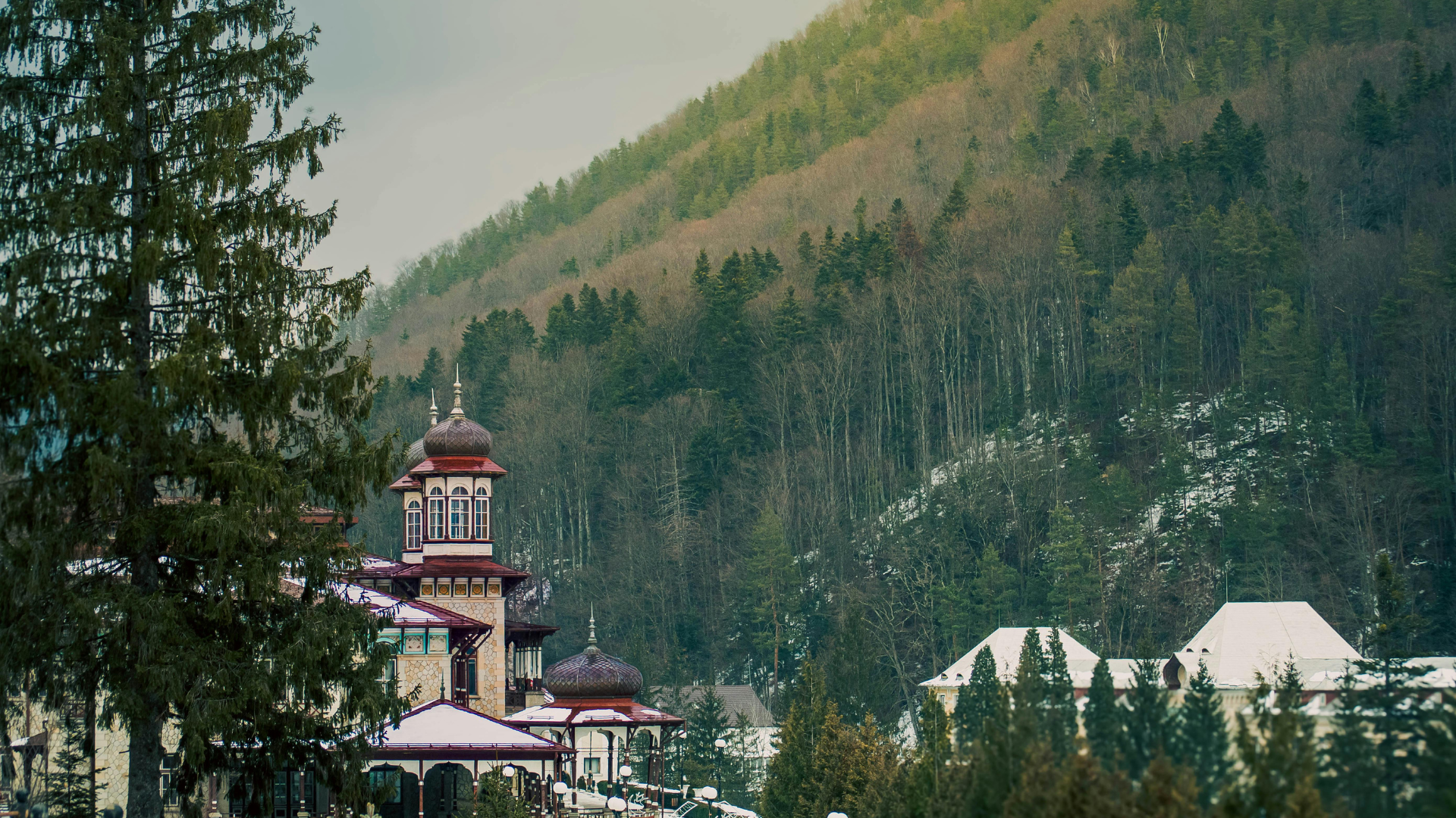 Church with onion dome and spires, surrounded by trees and mountain in the background.
