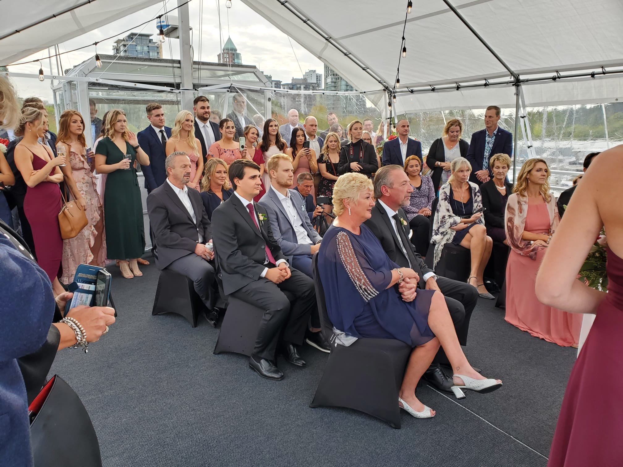 Group of people dressed formally attending an event in a tent with city skyline in the background.