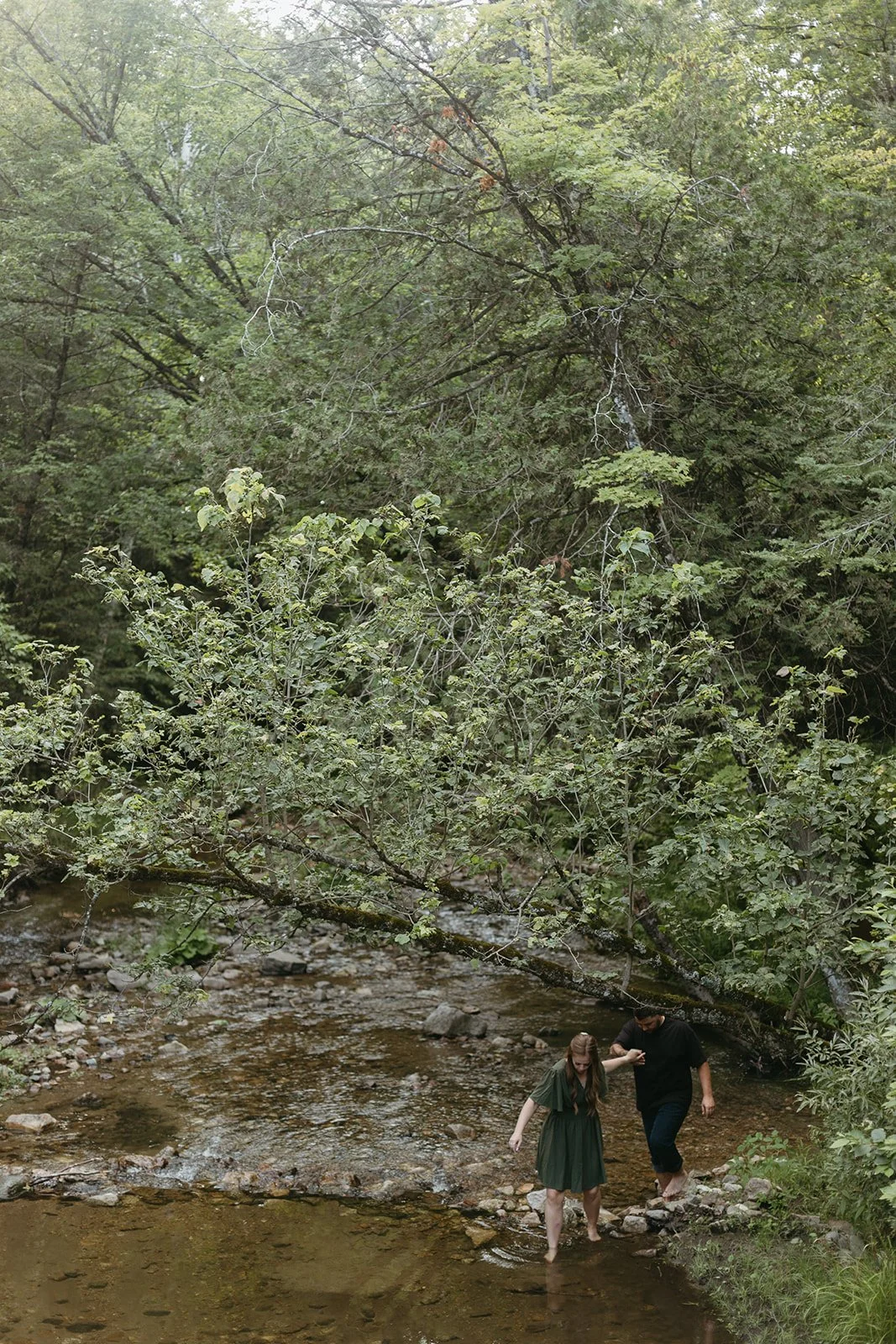 Couple walks in a creek during their engagement session in Low, Quebec