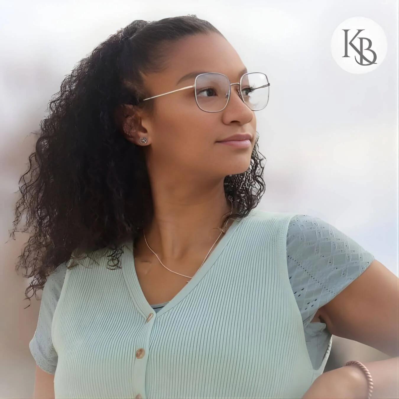 Karissa Bass, the owner of KayB Wellness, posed with one arm resting on railing and head turned looking over her right shoulder, wearing a light green sweater vest and light green short sleeve blouse underneath.