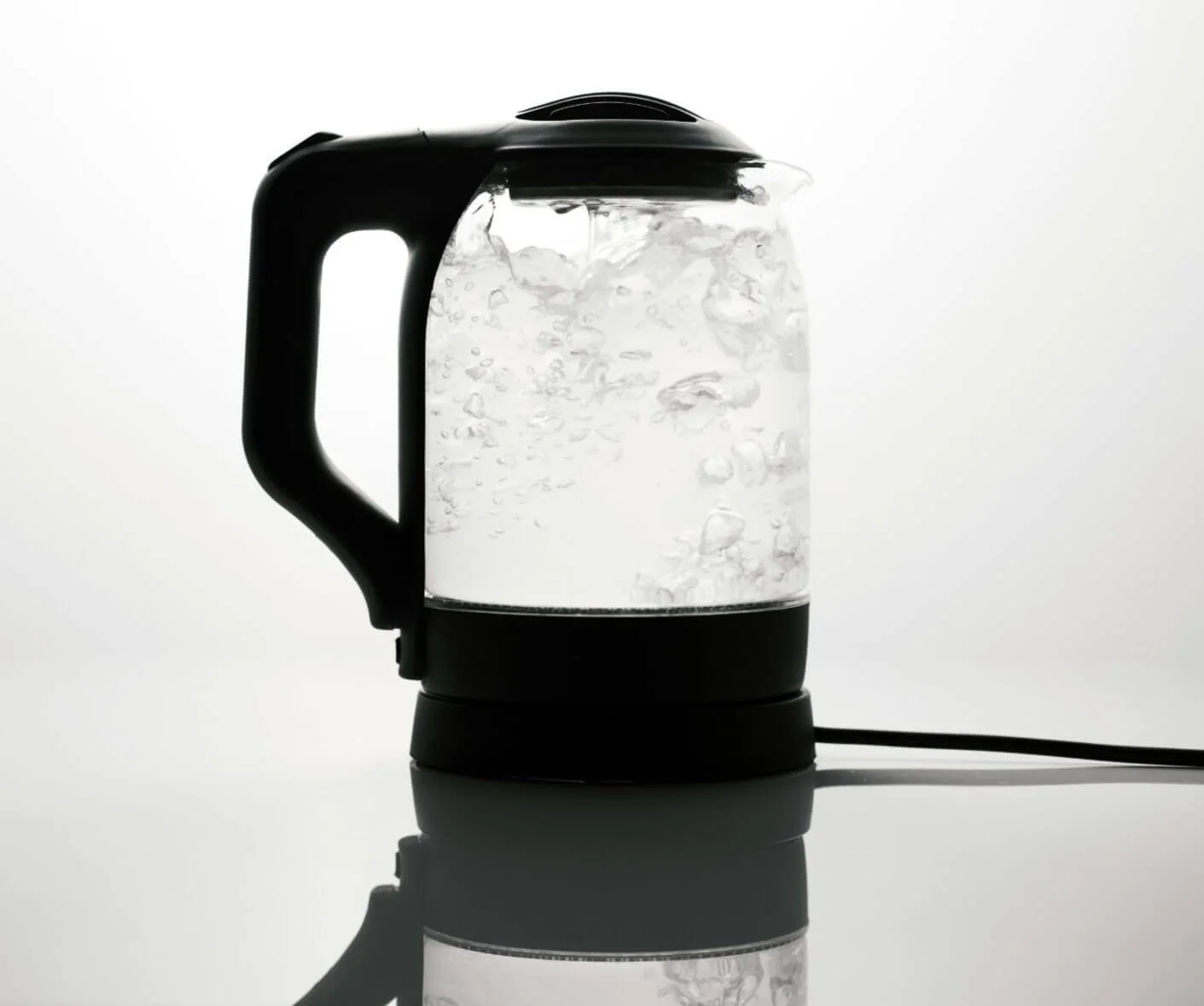 Electric kettle boiling water with bubbles, on a reflective surface against a white background.