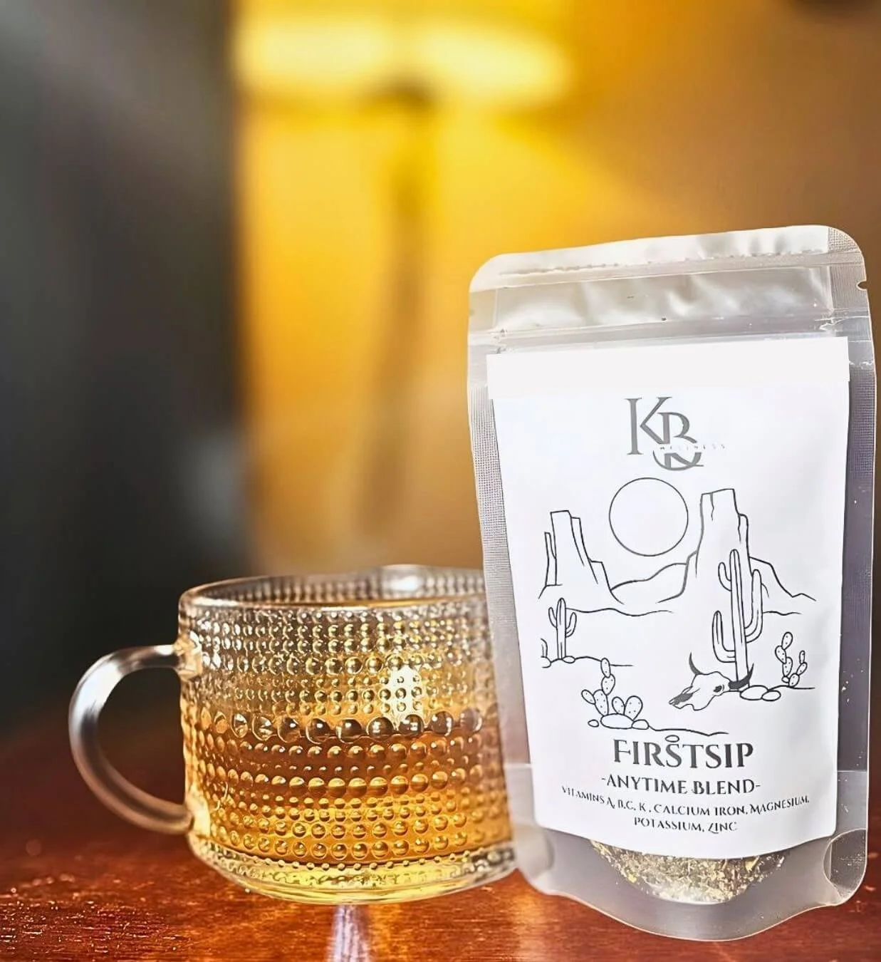 First Sip herbal tea in package  sitting next to a cup full of tea on a wooden table.